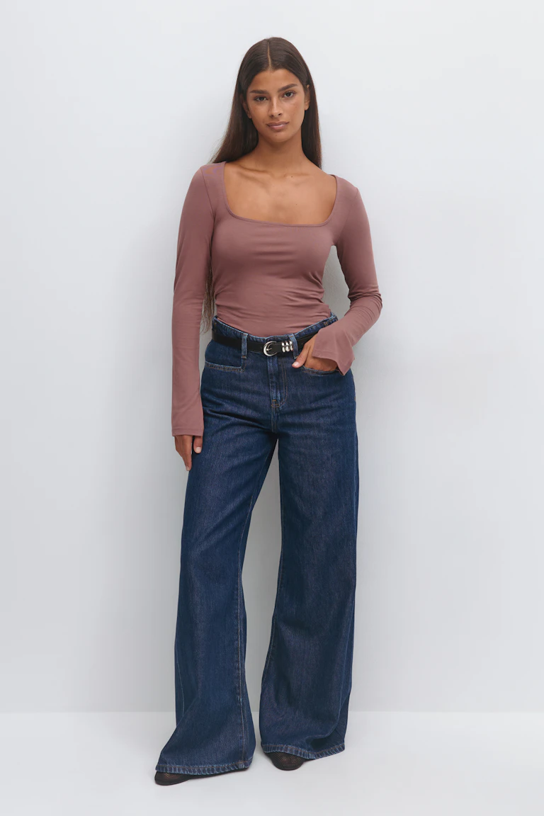 Mauve long-sleeve square-neck fitted top gecombineerd met een high-waist dark indigo wide-leg jeans, zwarte leren riem met zilveren gesp met dubbele ring en spitse zwarte schoenen.