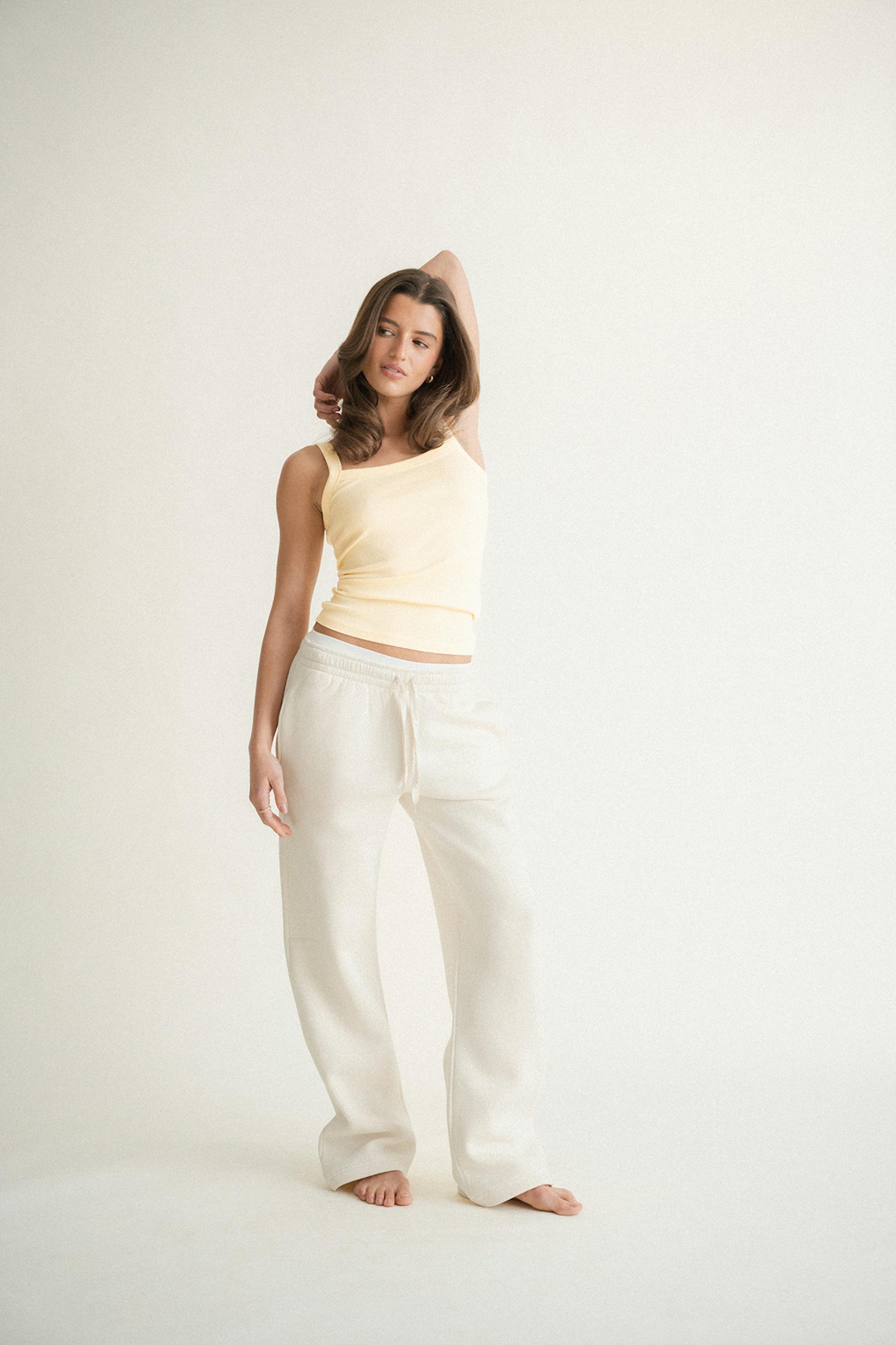 Light yellow asymmetrical tank top paired with cream drawstring wide-leg lounge pants.