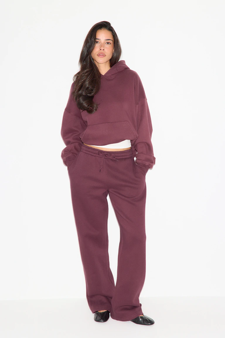 En vinröd, kort hoodie med känguruficka, i kombination med matchande vinröda joggingbyxor med dragsko och svarta ballerinaskor; en vit linne syns i midjan.