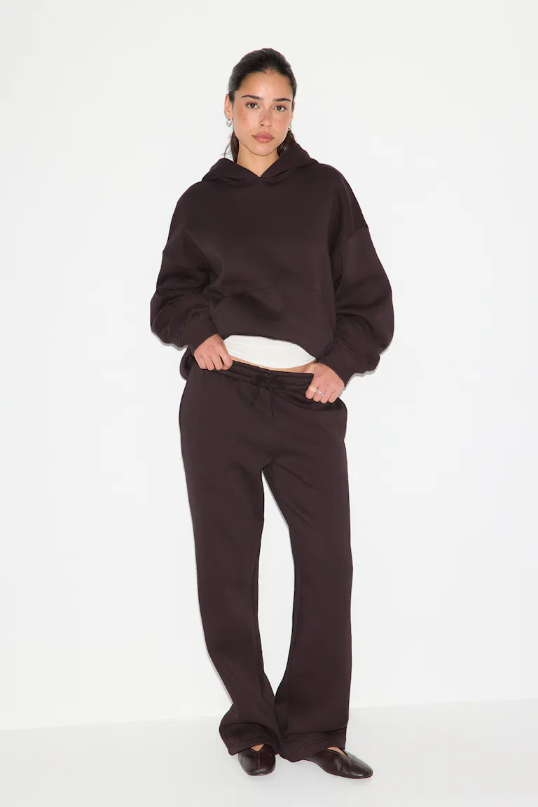 En oversized, mørkebrun hettegenser over en hvit tank-top, kombinert med mørkebrune joggebukser med snøring og brune skinnballerinasko.
