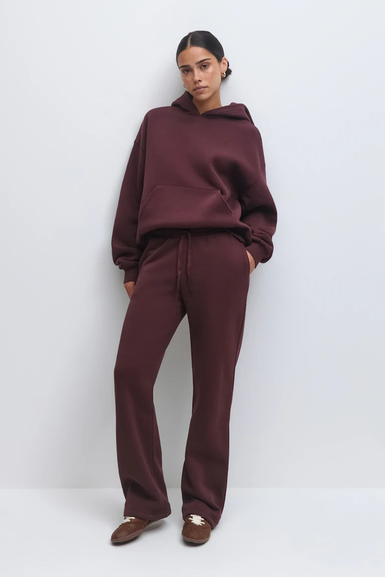 Ensemble de vêtements d'intérieur bordeaux assortis : sweat à capuche surdimensionné avec poche kangourou associé à un pantalon de survêtement à taille droite et cordon de serrage, le tout assorti de chaussures à enfiler de style mocassin marron.