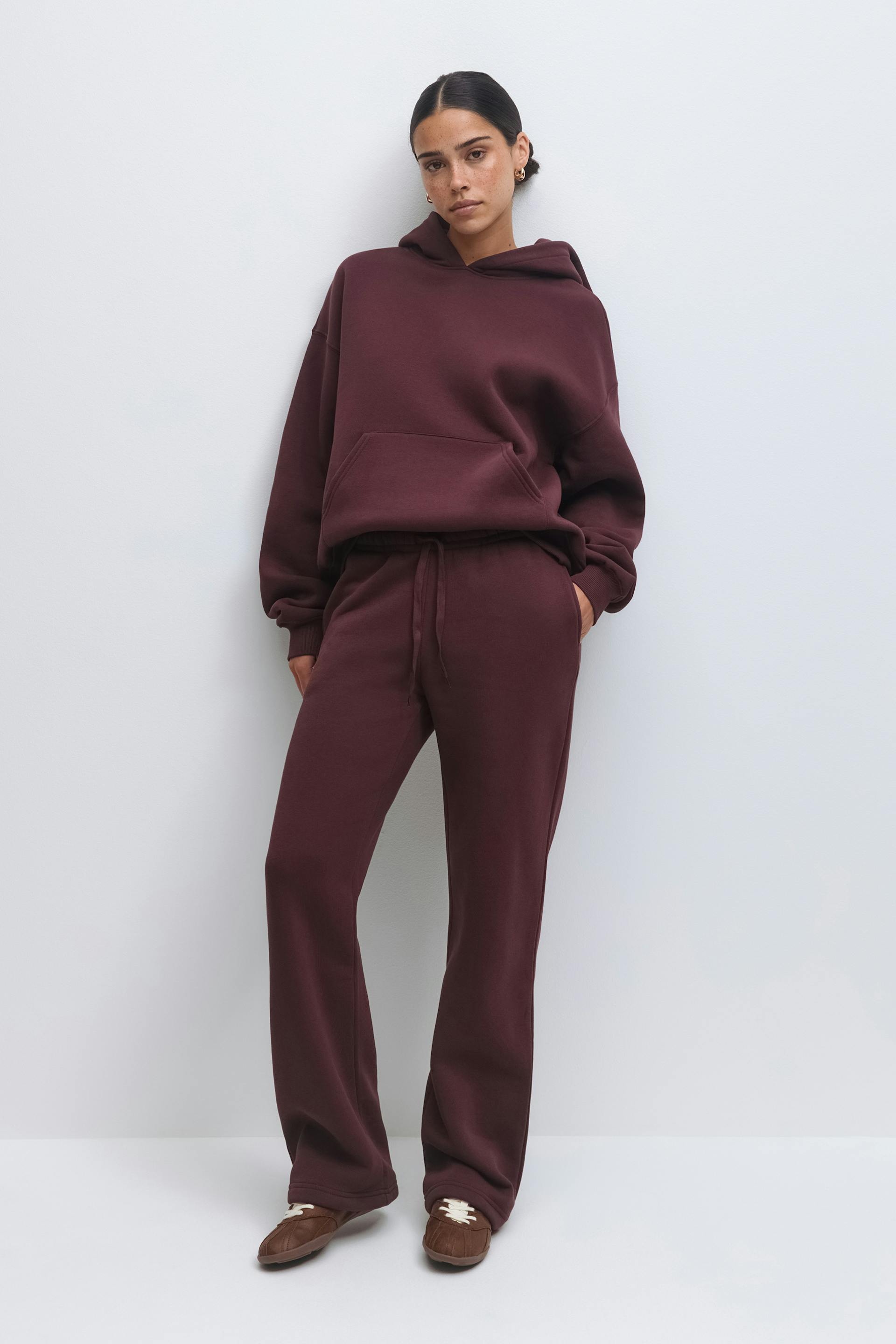 Matching burgundy loungewear set: oversized hoodie with kangaroo pocket paired with drawstring-waist straight-leg sweatpants, styled with brown moccasin-style slip-on shoes.