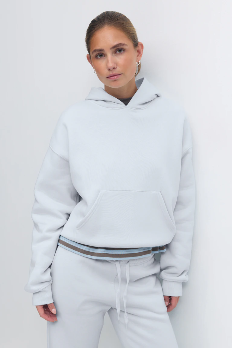 Lichtblauw oversized sweatshirt met capuchon, kangoeroezak en geribde boorden, gelaagd over een gestreepte zoomband, gecombineerd met een bijpassende lichtblauwe joggingbroek met koord.