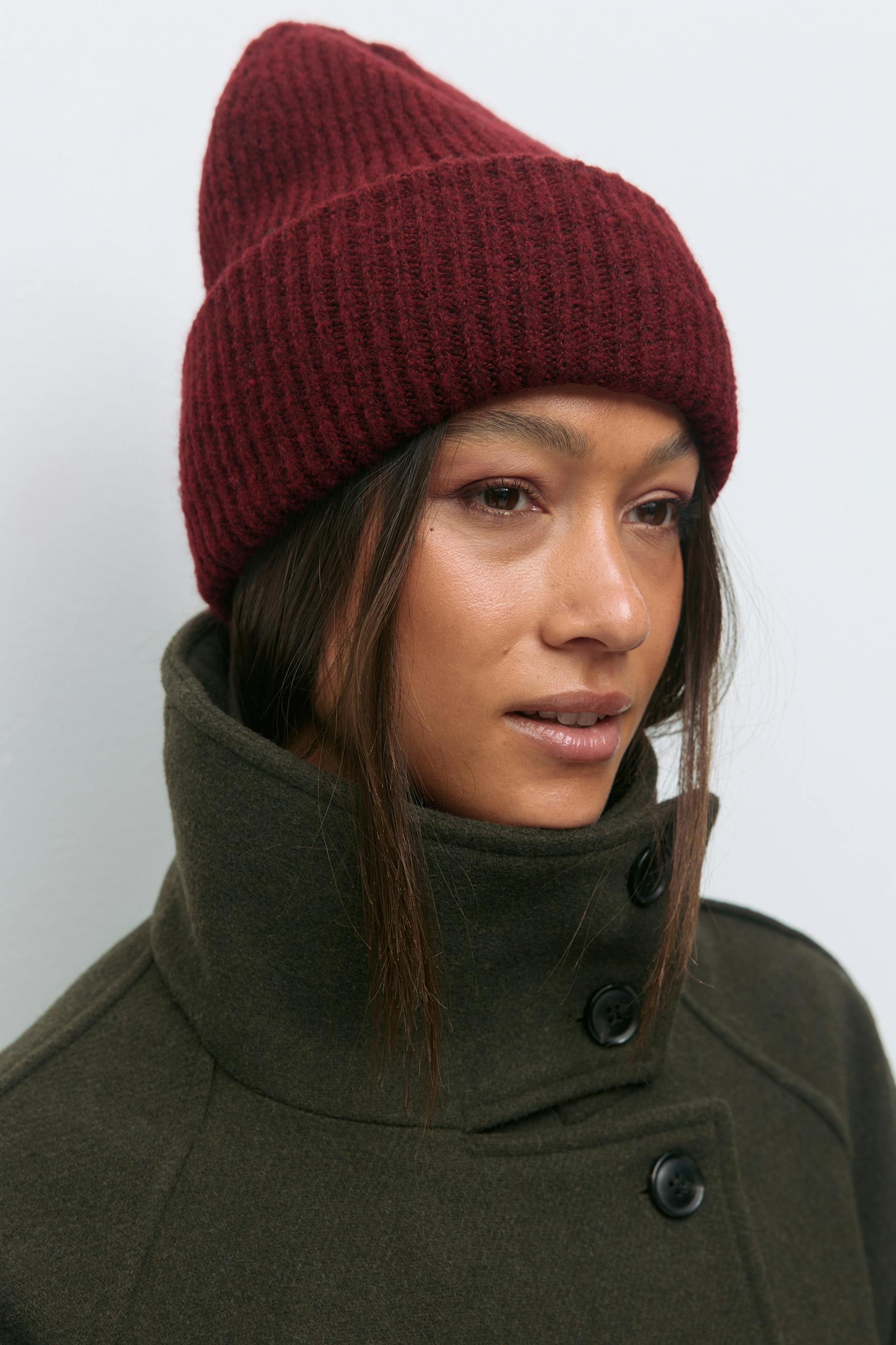 Burgundinpunainen neulepipo ja tummanoliivinvärinen korkeakauluksinen villatakki, jossa on mustat napit.