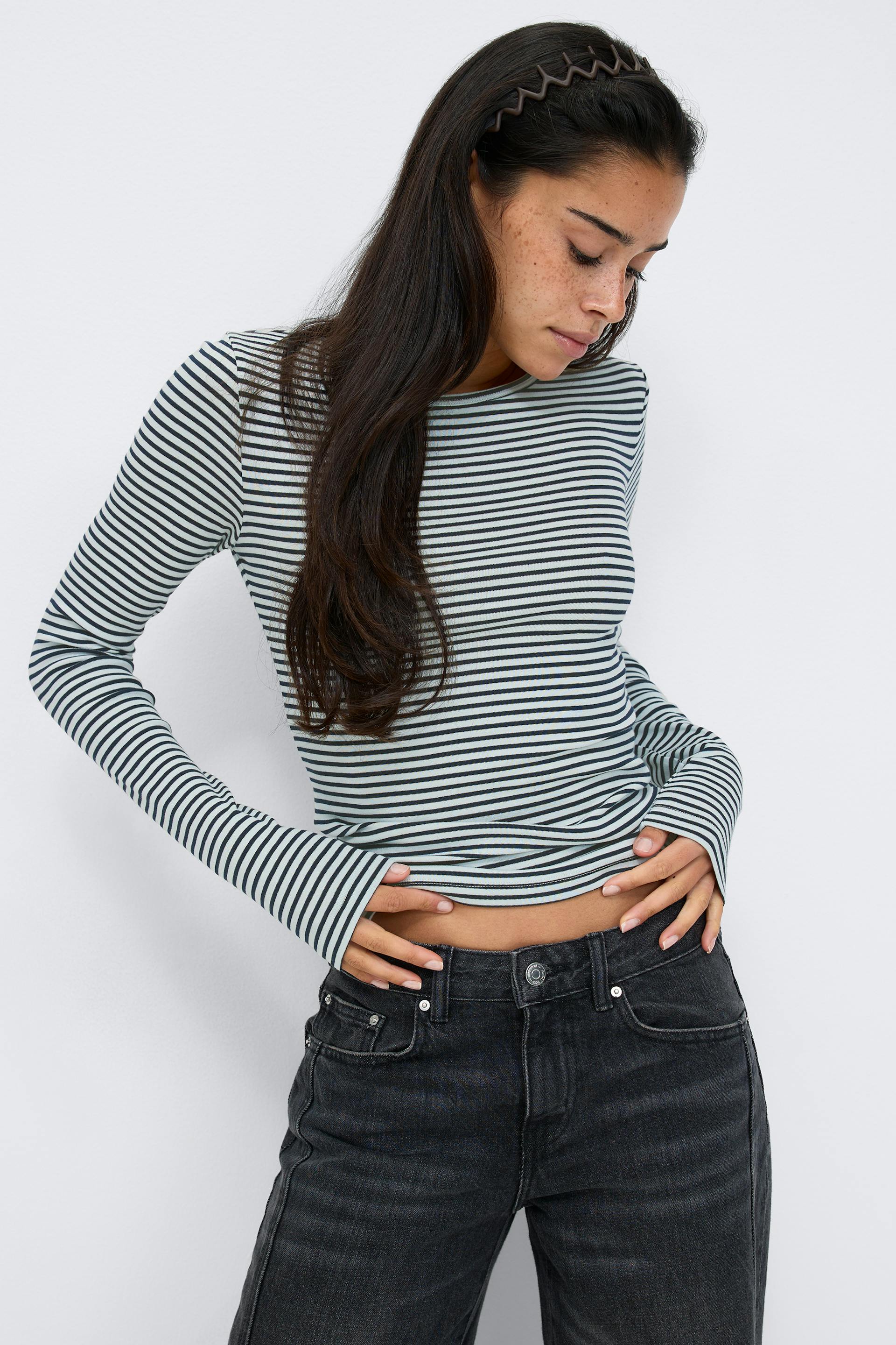 Fitted long-sleeve crewneck top with narrow black-and-white horizontal stripes, paired with high-waisted washed black denim jeans.