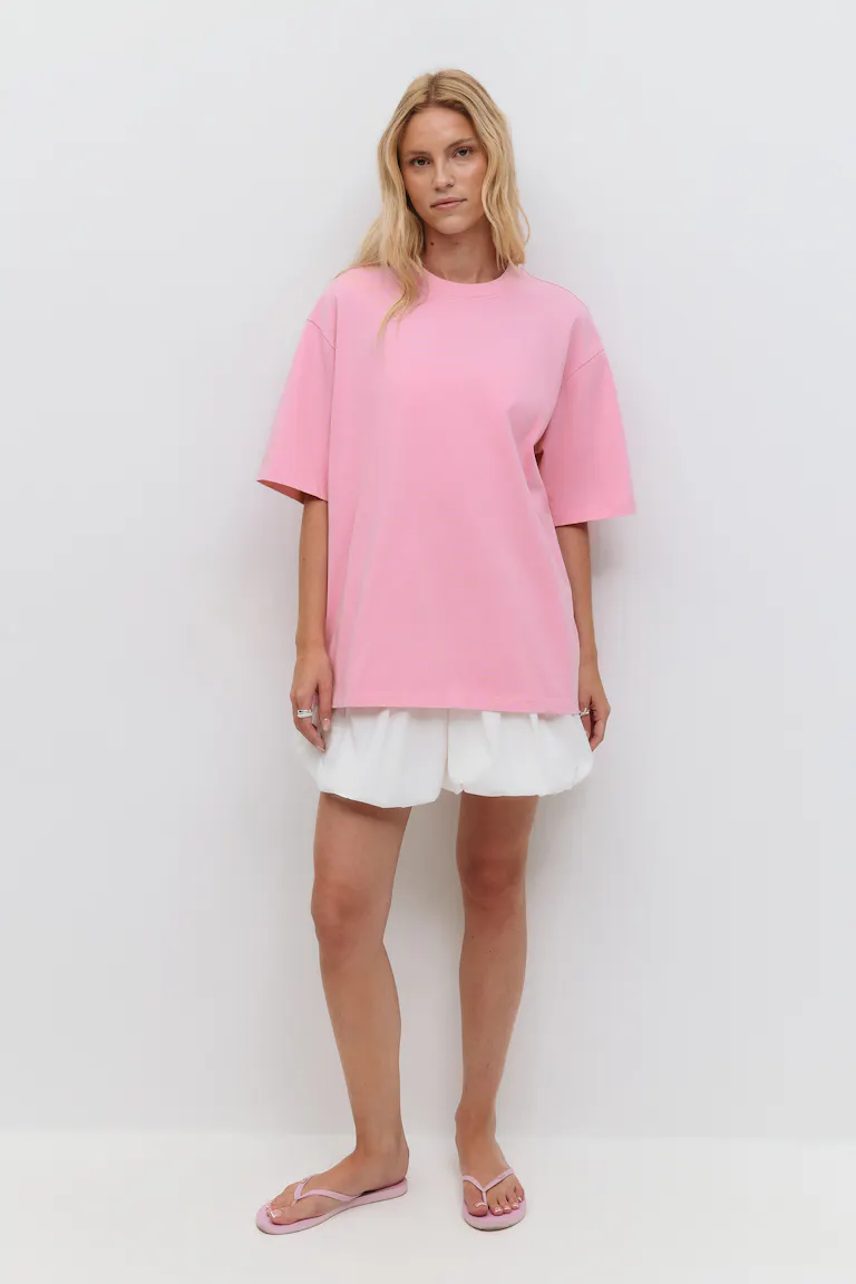 Pastelrosa oversized kortærmet T-shirt med rund hals kombineret med hvide shorts med boblekant og lyserøde sandaler med klipklapper.