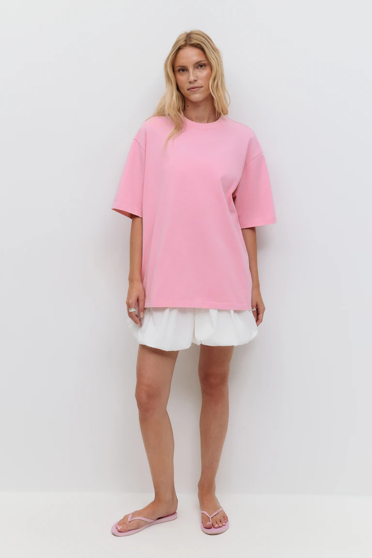 Pastelrosa oversized kortærmet T-shirt med rund hals kombineret med hvide shorts med boblekant og lyserøde sandaler med klipklapper.