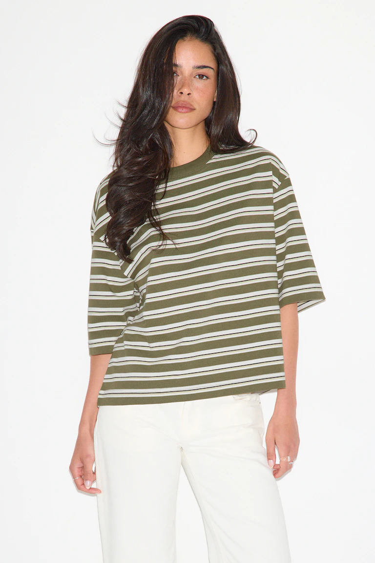 T-shirt oversize à manches courtes, col rond, rayé horizontalement en vert olive et blanc, associé à un pantalon droit blanc cassé.