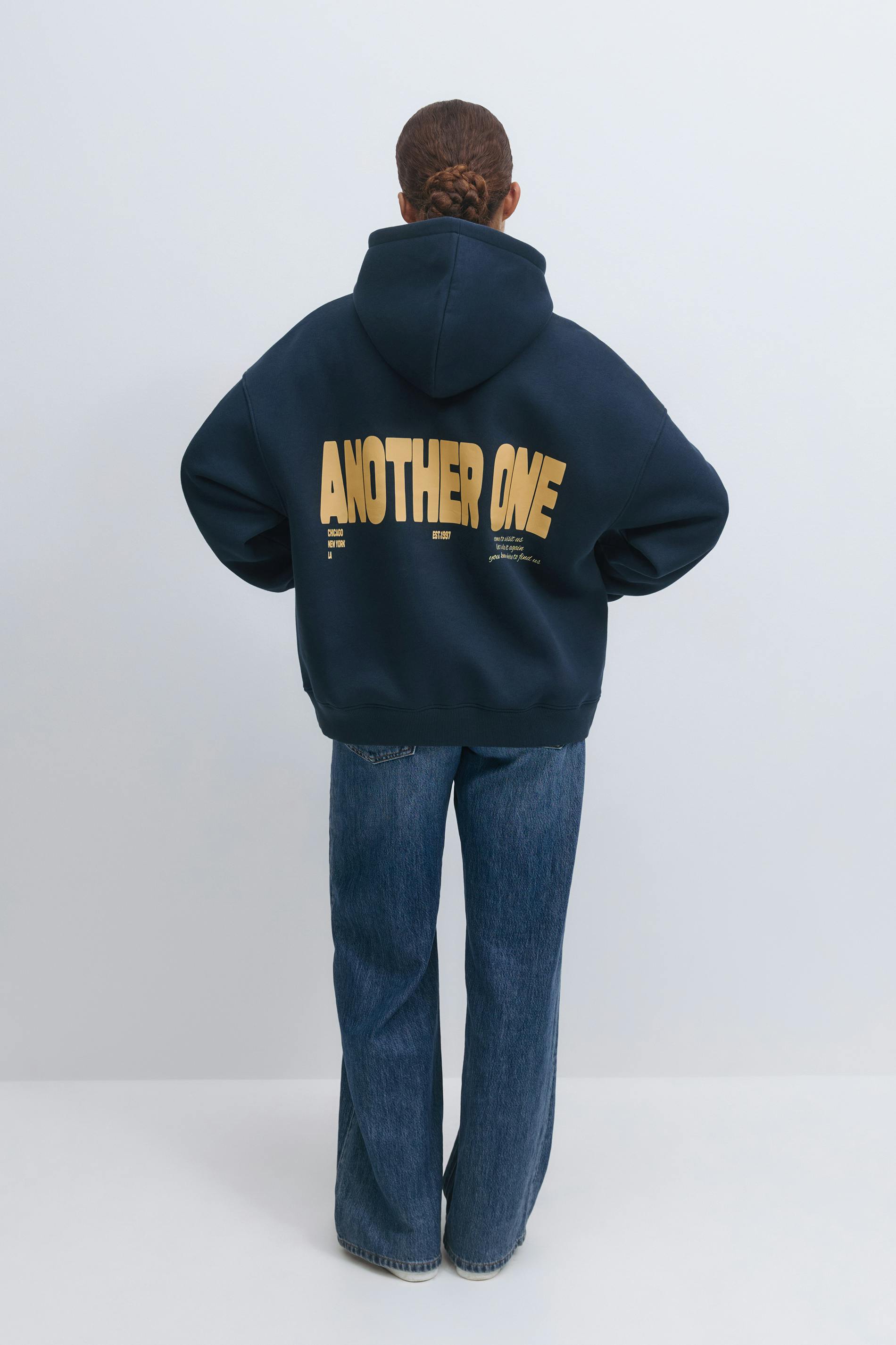 Navy oversized hooded sweatshirt featuring a large yellow "ANOTHER ONE" back print, paired with straight-leg medium-blue denim jeans.