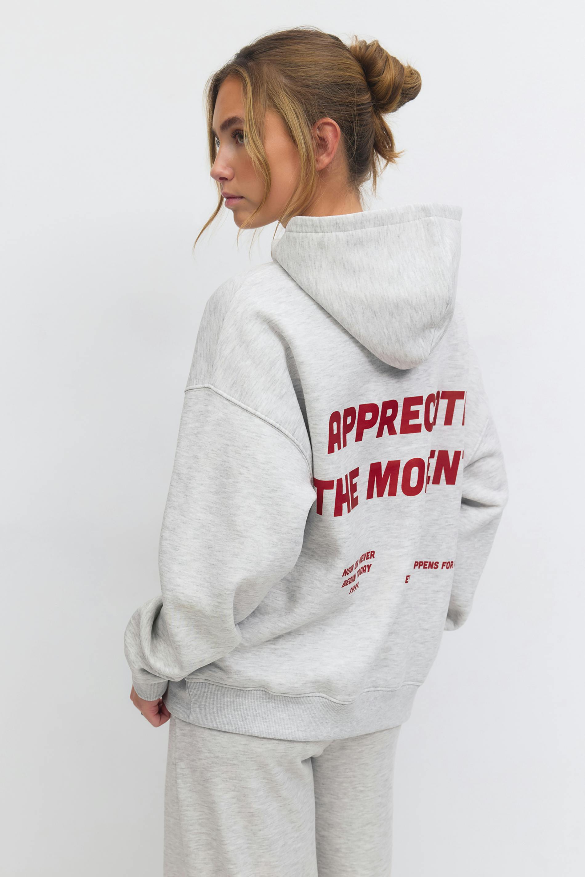 Light heather-gray oversized hooded sweatshirt with red block lettering on the back, paired with matching heather-gray sweatpants.