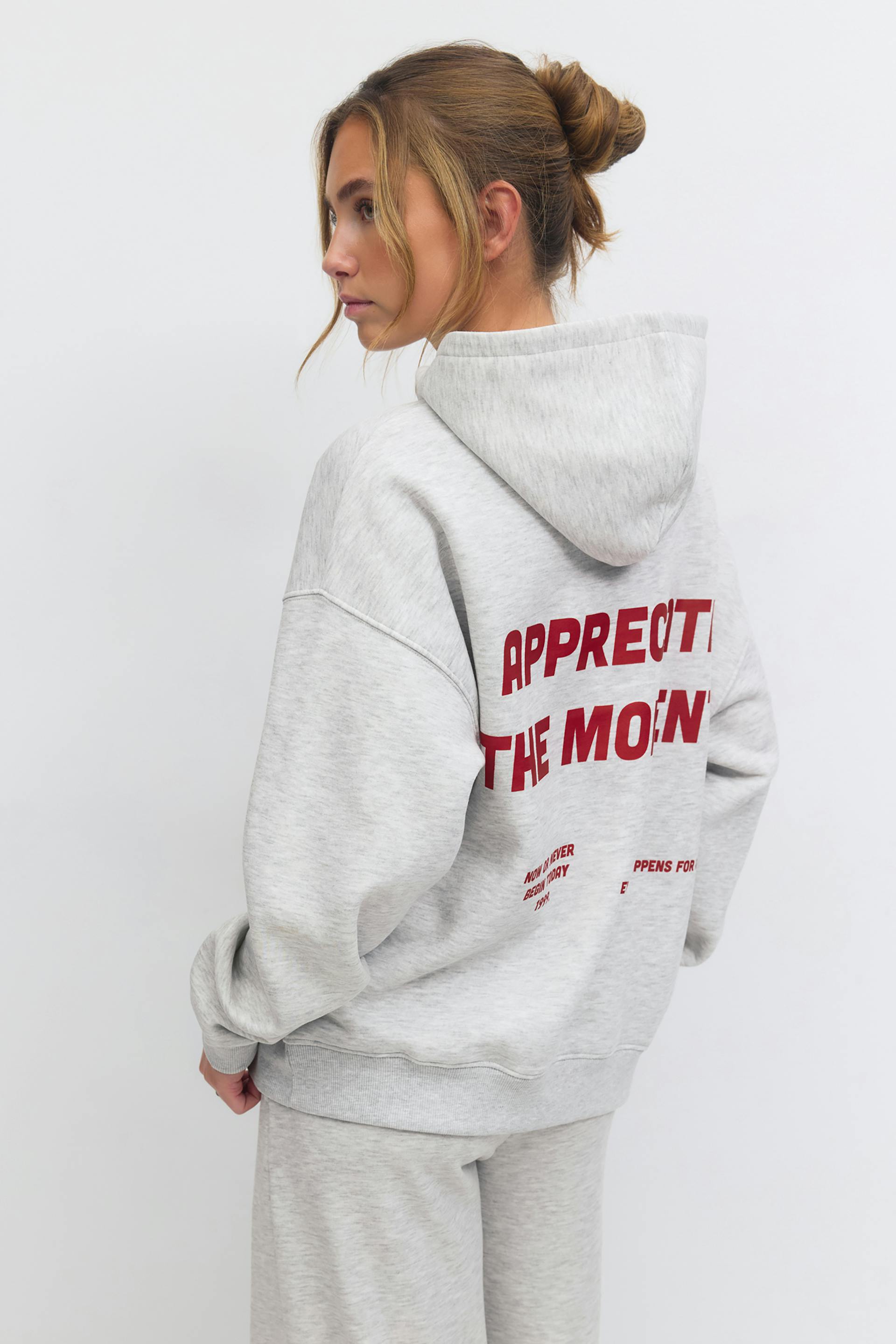 Light heather-gray oversized hooded sweatshirt with red block lettering on the back, paired with matching heather-gray sweatpants.