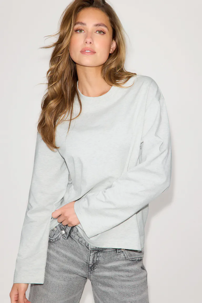Avslappnad ljus ljunggrå crewneck med lång ärm kombinerad med blekgrå jeans med hög midja.