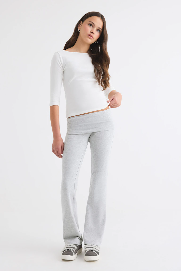 Fitted white long-sleeve top with light grey flared trousers and grey slip-on sneakers.