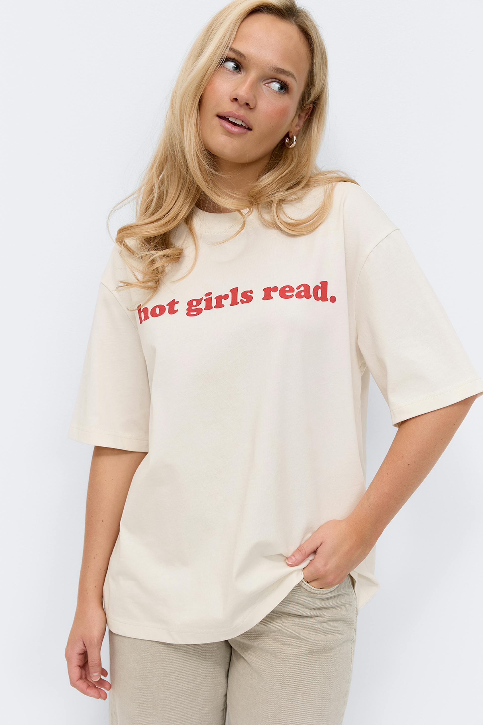 Kermanvärinen ylimitoitettu lyhythihainen T-paita, jossa on punainen "hot girls read." teksti rinnassa, yhdistettynä vaaleanbeigeihin housuihin.