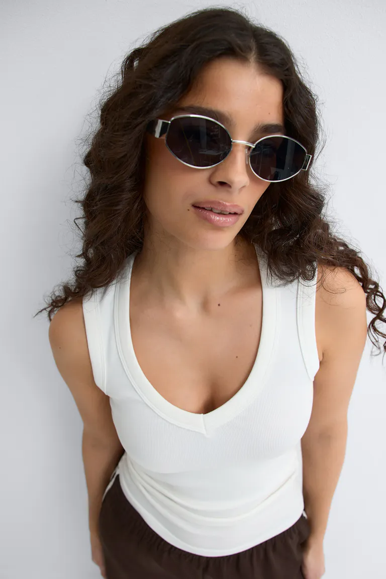 Top noir côtelé à manches longues, pantalon en denim indigo foncé, petites boucles d'oreilles argentées et lunettes de soleil rondes à monture argentée et miroir.
