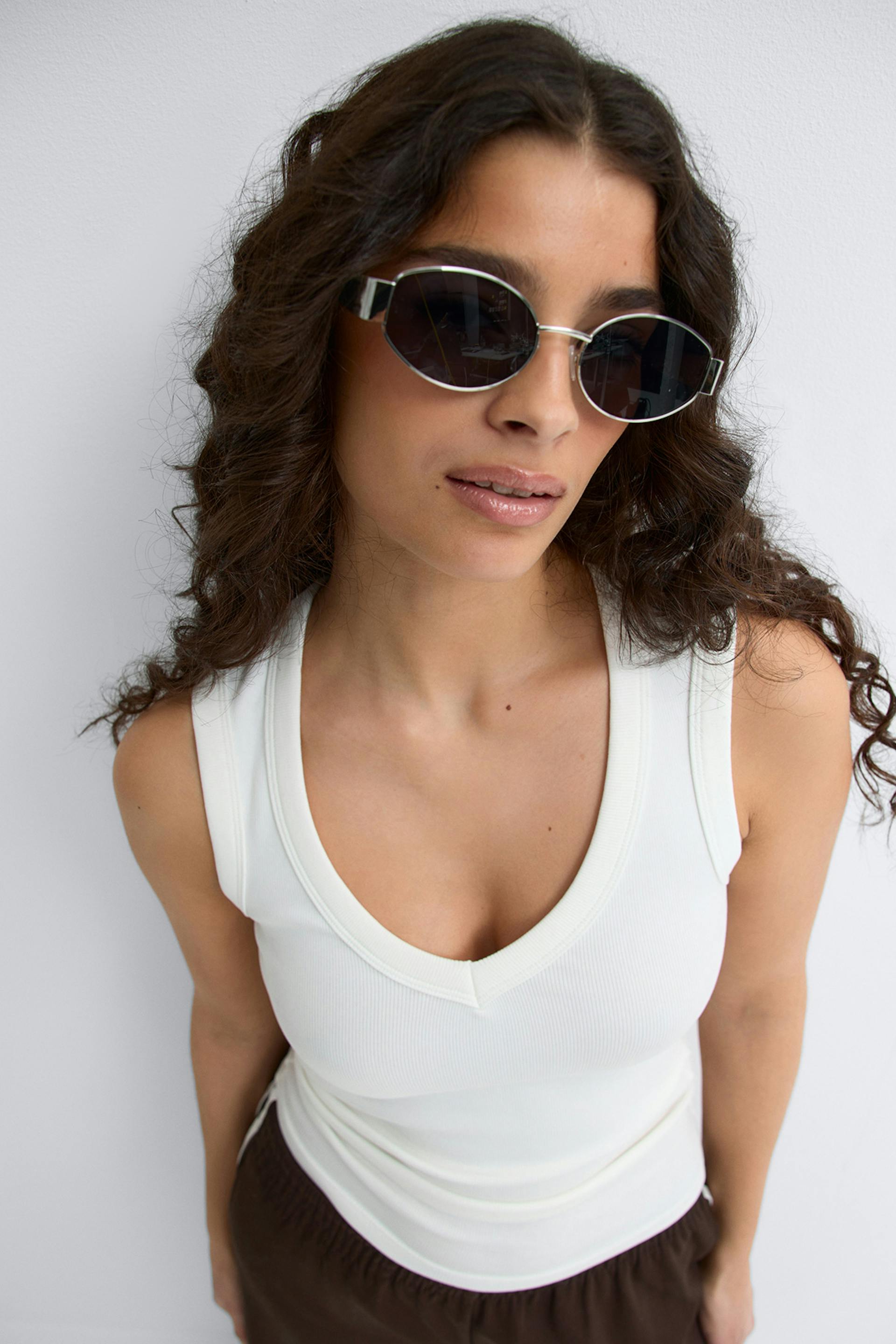 Black ribbed long-sleeve top, dark indigo denim trousers, small silver hoop earrings, and round silver-framed mirrored sunglasses.