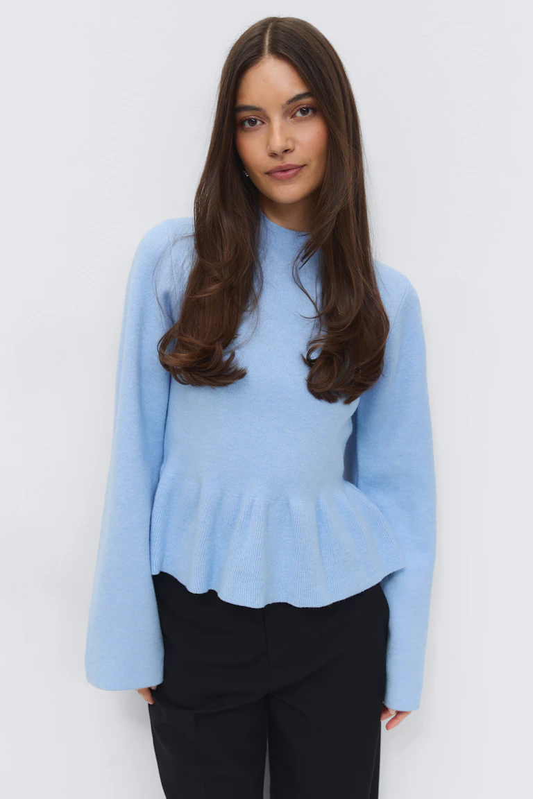 Hellblauer, langärmeliger Strickpullover mit Rundhalsausschnitt und Schößchensaum, kombiniert mit einer schwarzen, taillierten Hose.