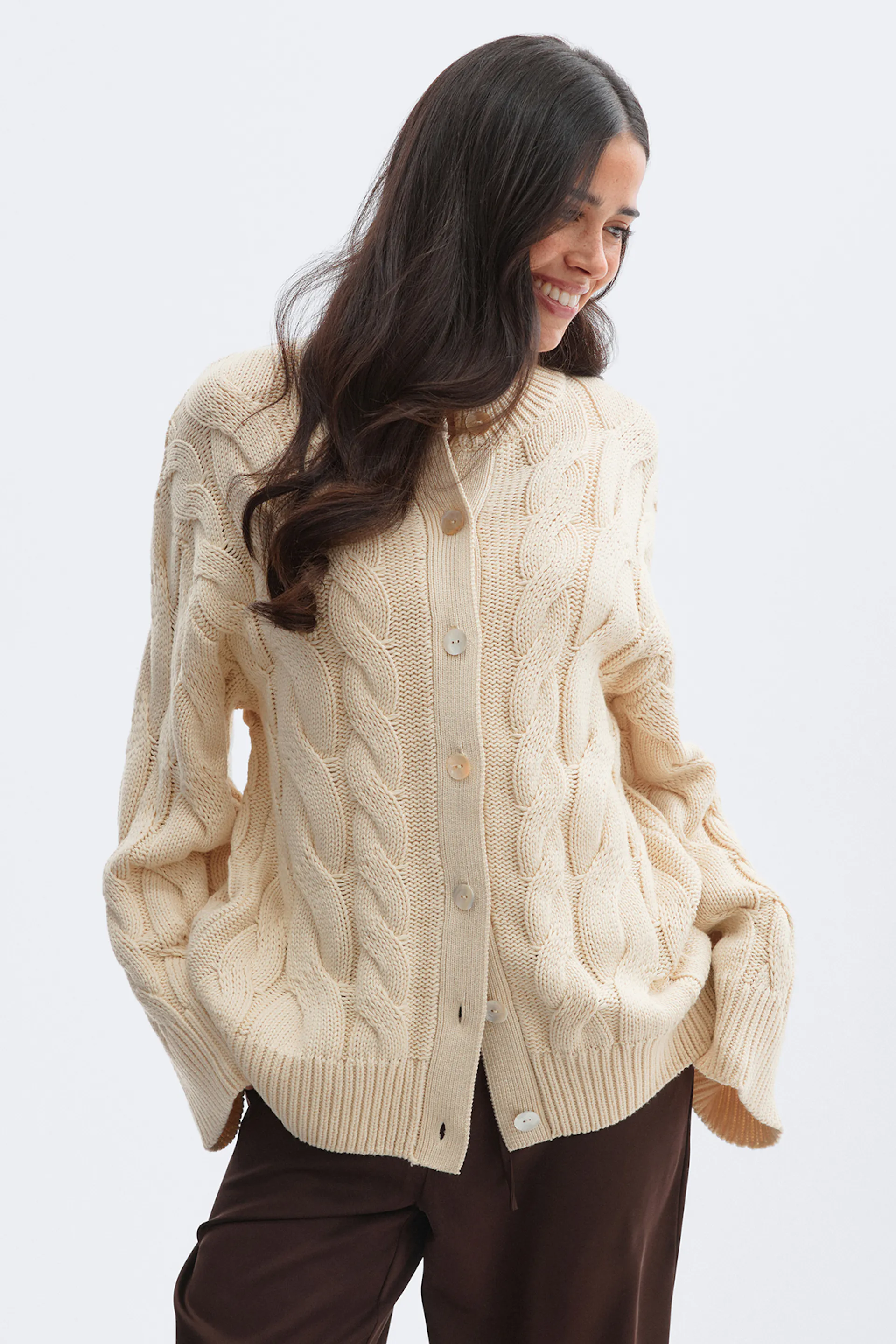 Cremefarbene Strickjacke mit Knopfleiste und gerippten Bündchen und Saum, kombiniert mit einer dunkelbraunen Hose.