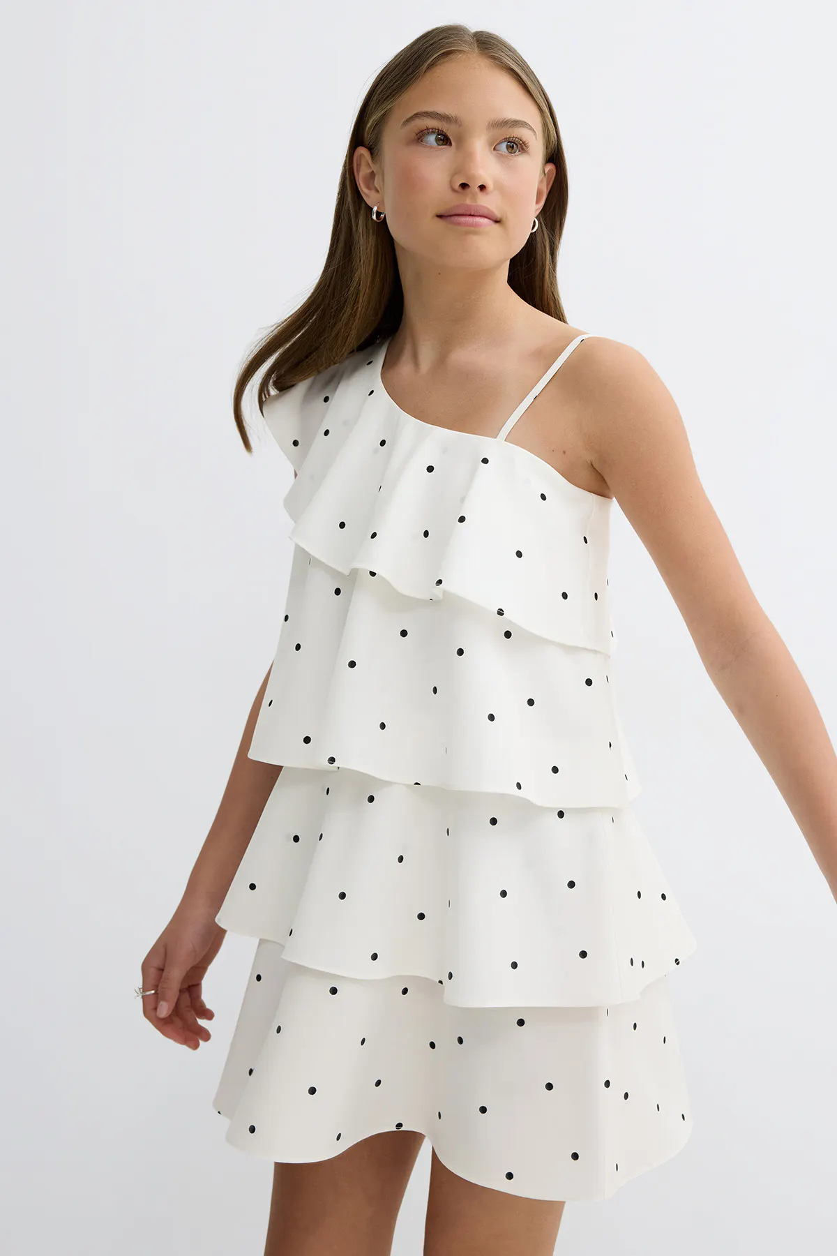 Robe blanche sans manches, à pois noirs, à volants asymétriques sur le corsage et à fine bretelle spaghetti.