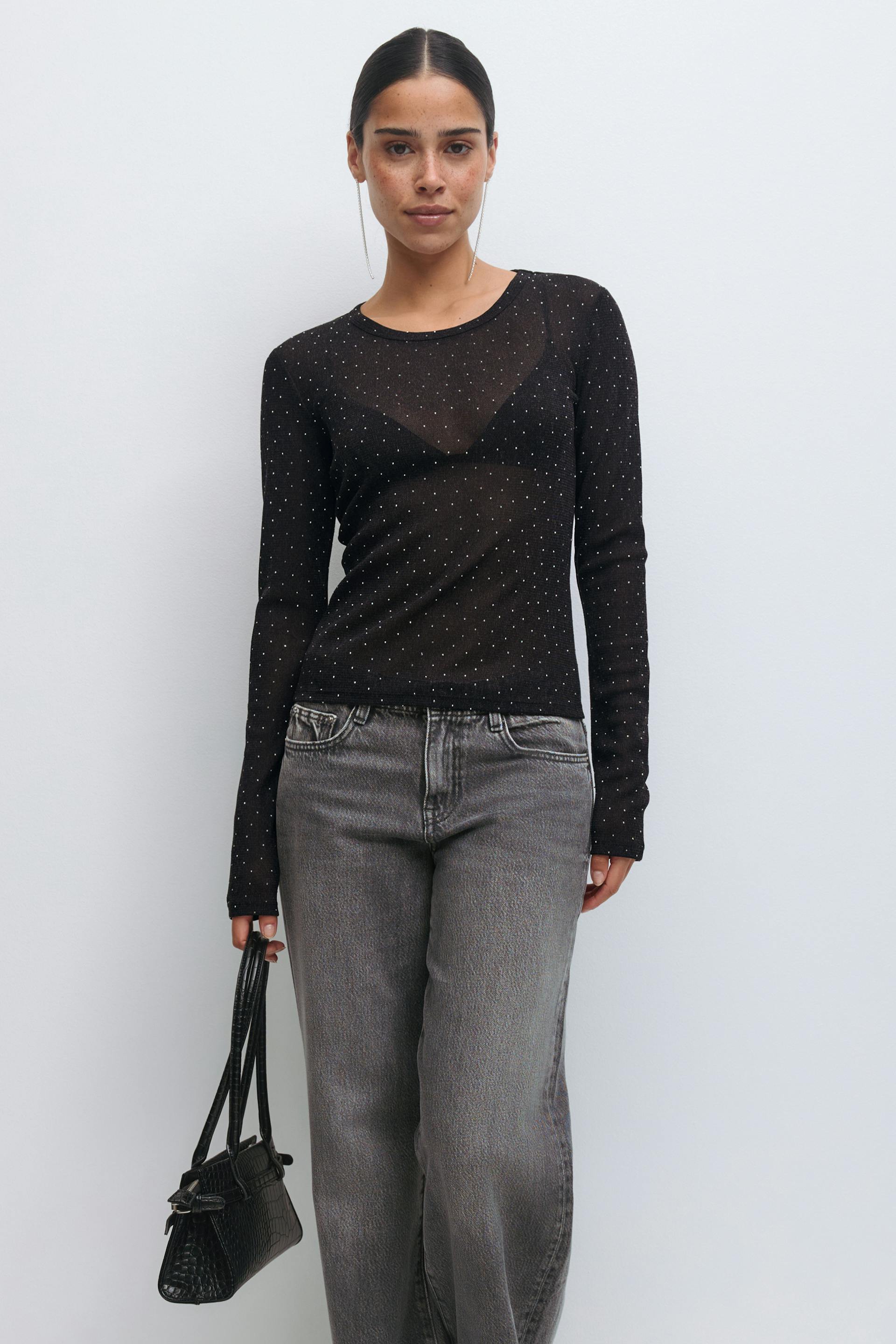 Skir svart långärmad topp med små metalliska prickar över en svart triangelbralette, blekgrå högmidjade jeans med raka ben, liten svart krokpräglad handväska och långa örhängen.