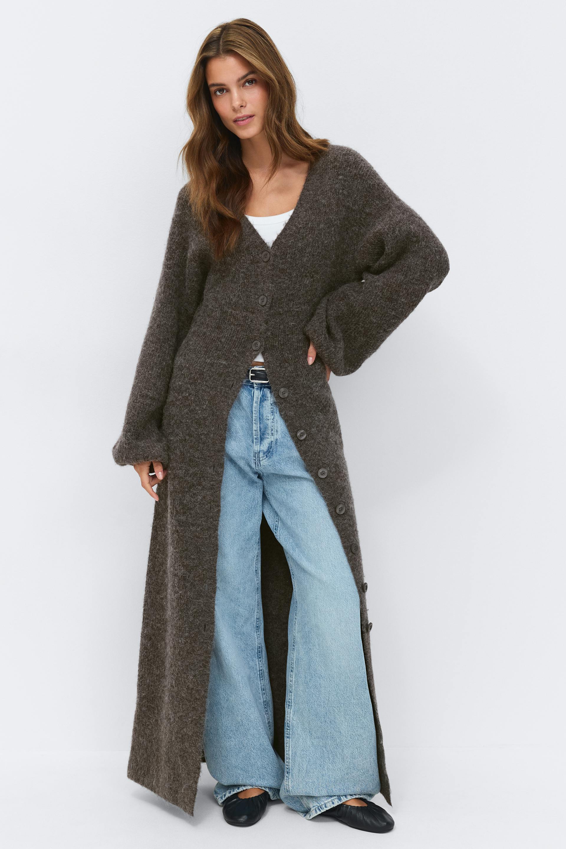 Donker antraciet geborstelde gebreide maxi-cardiganjurk met V-hals en lange ballonmouwen, gecombineerd met spitse pumps met zebraprint en zilveren oorbellen met schijfjes.