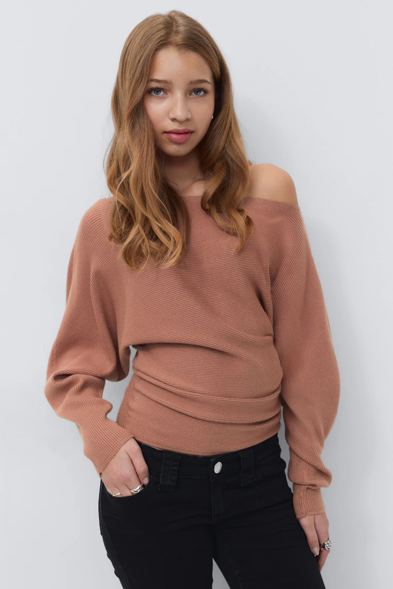 Langærmet sweater med off-the-shoulder-rib i støvet rose sammen med højtaljede sorte skinny jeans og sølvringe.
