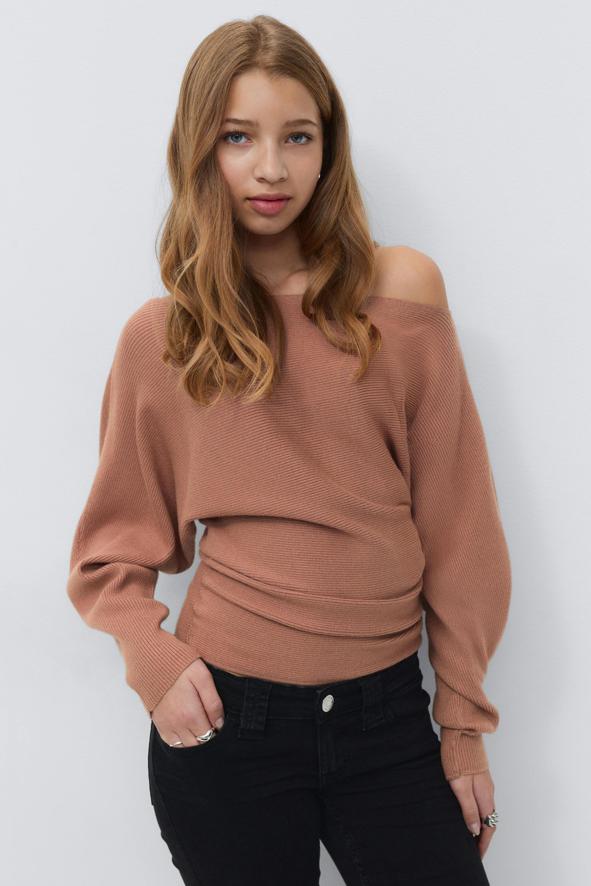 Off-the-shoulder ribbed long-sleeve sweater in dusty rose paired with high-waisted black skinny jeans and silver rings.