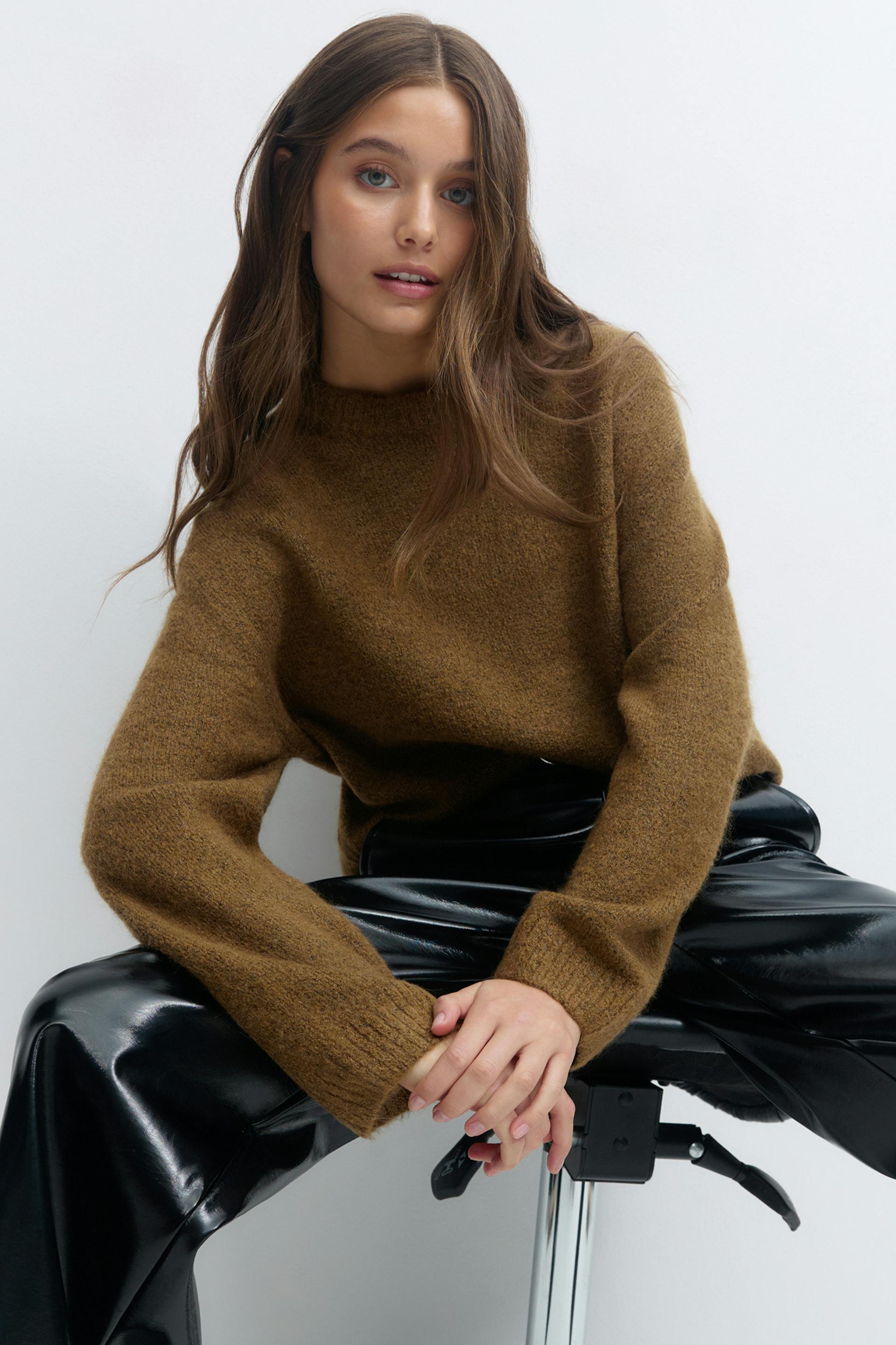 Brown textured crew-neck sweater with long sleeves paired with black patent-leather wide-leg trousers.