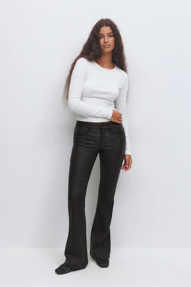 White fitted long-sleeve crew-neck top paired with black high-rise faux-leather flared trousers and black ballet flats.