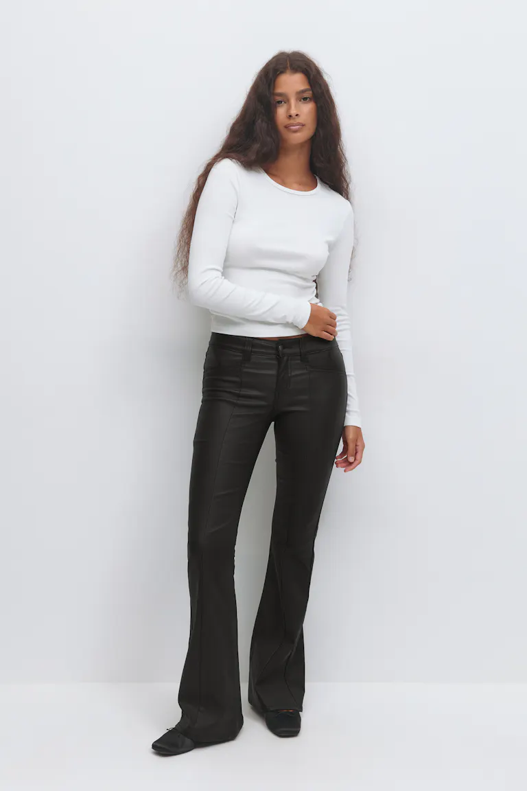 White fitted long-sleeve crew-neck top paired with black high-rise faux-leather flared trousers and black ballet flats.