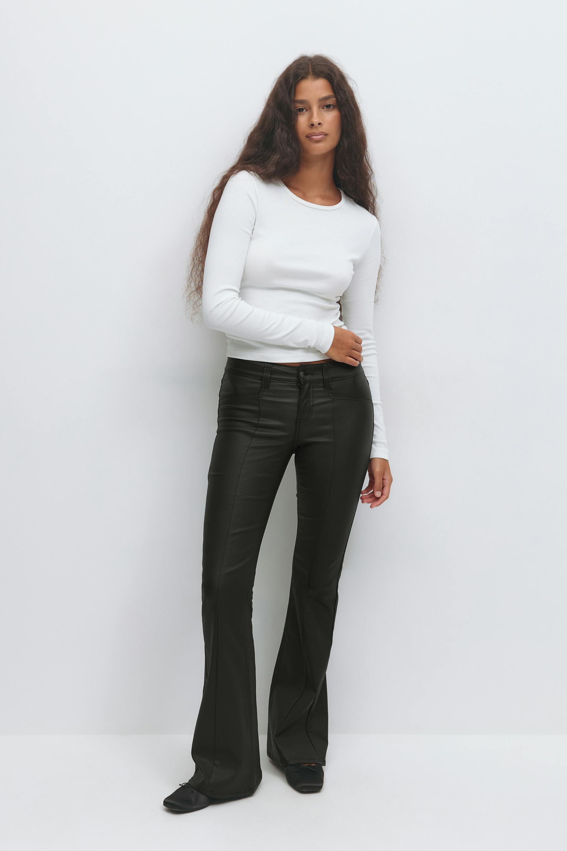 Valkoinen, pitkähihainen, pitkähihainen yläosa, johon on yhdistetty mustat korkeavyötäröiset tekonahkaiset levenevät housut ja mustat balettitossut.