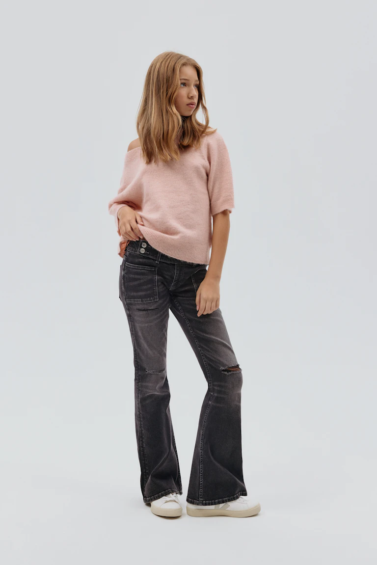 Pink off-the-shoulder short-sleeve brushed-knit sweater; faded black flared jeans with knee distressing and front patch pockets; white low-top sneakers.