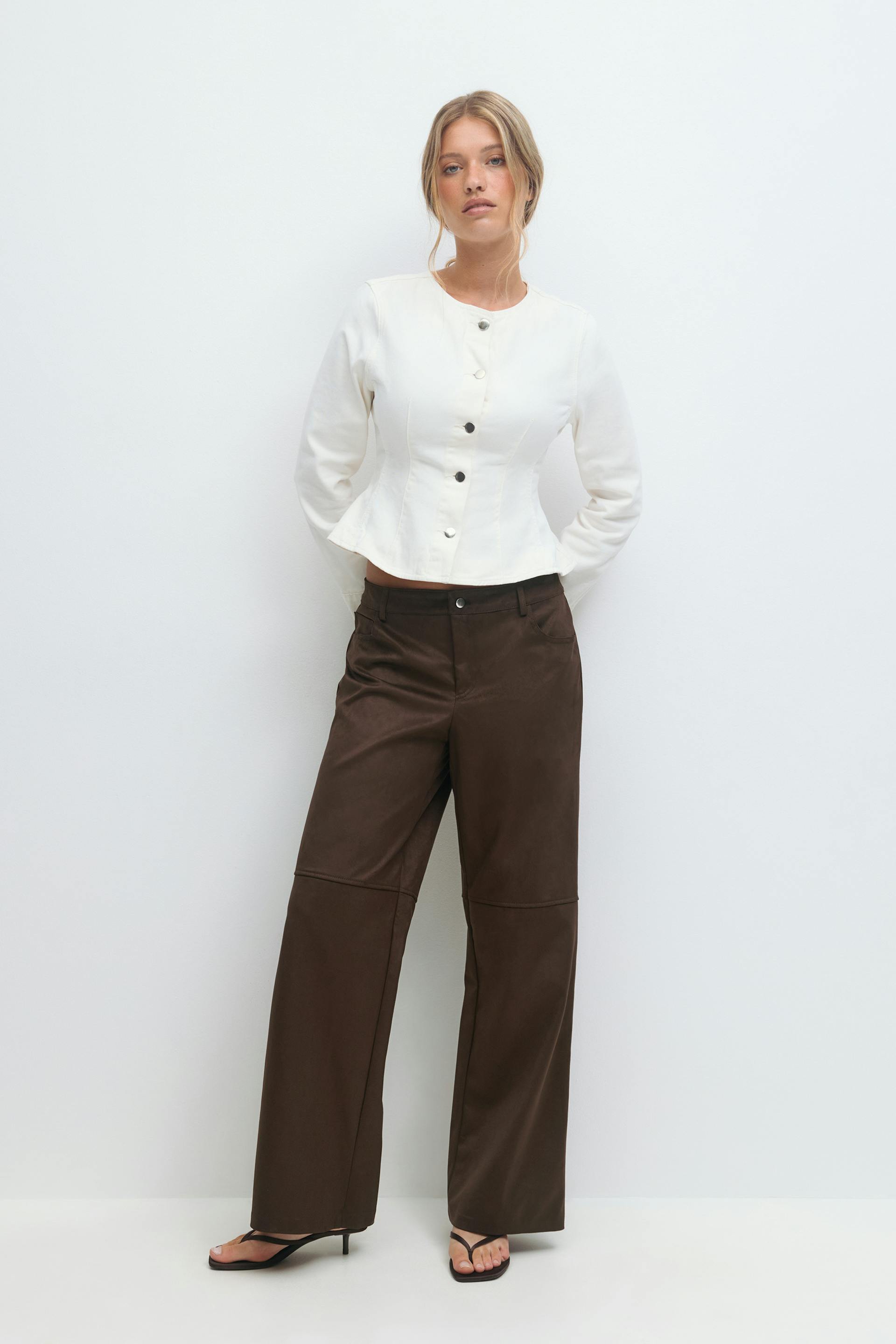 White fitted long-sleeve button-front peplum jacket; dark brown high-waisted wide-leg trousers with knee seam; black strappy heeled sandals.