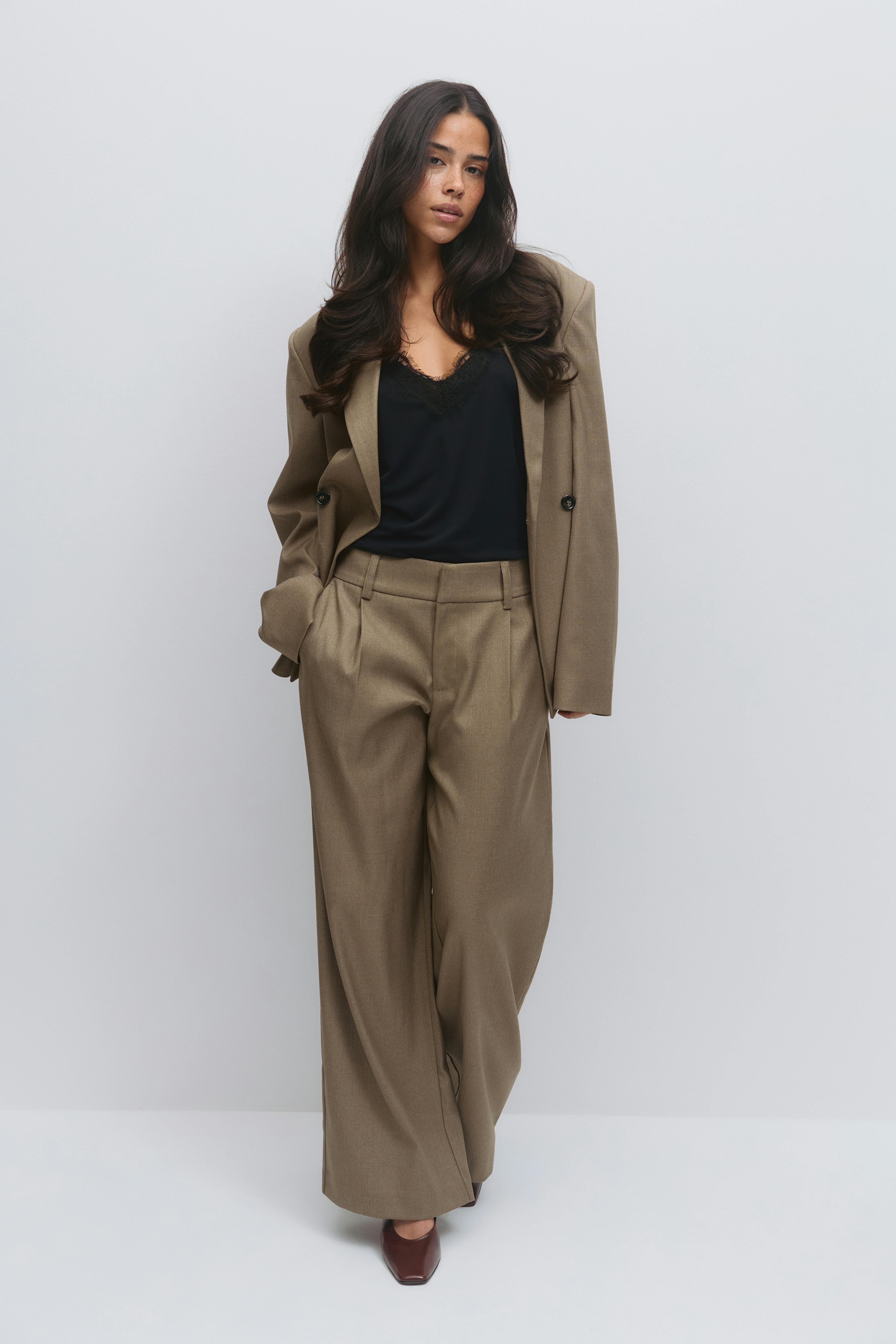 Model wearing a taupe double‑breasted tailored blazer with matching high‑waist, wide‑leg trousers, a black lace‑trim camisole, and brown square‑toe heels.