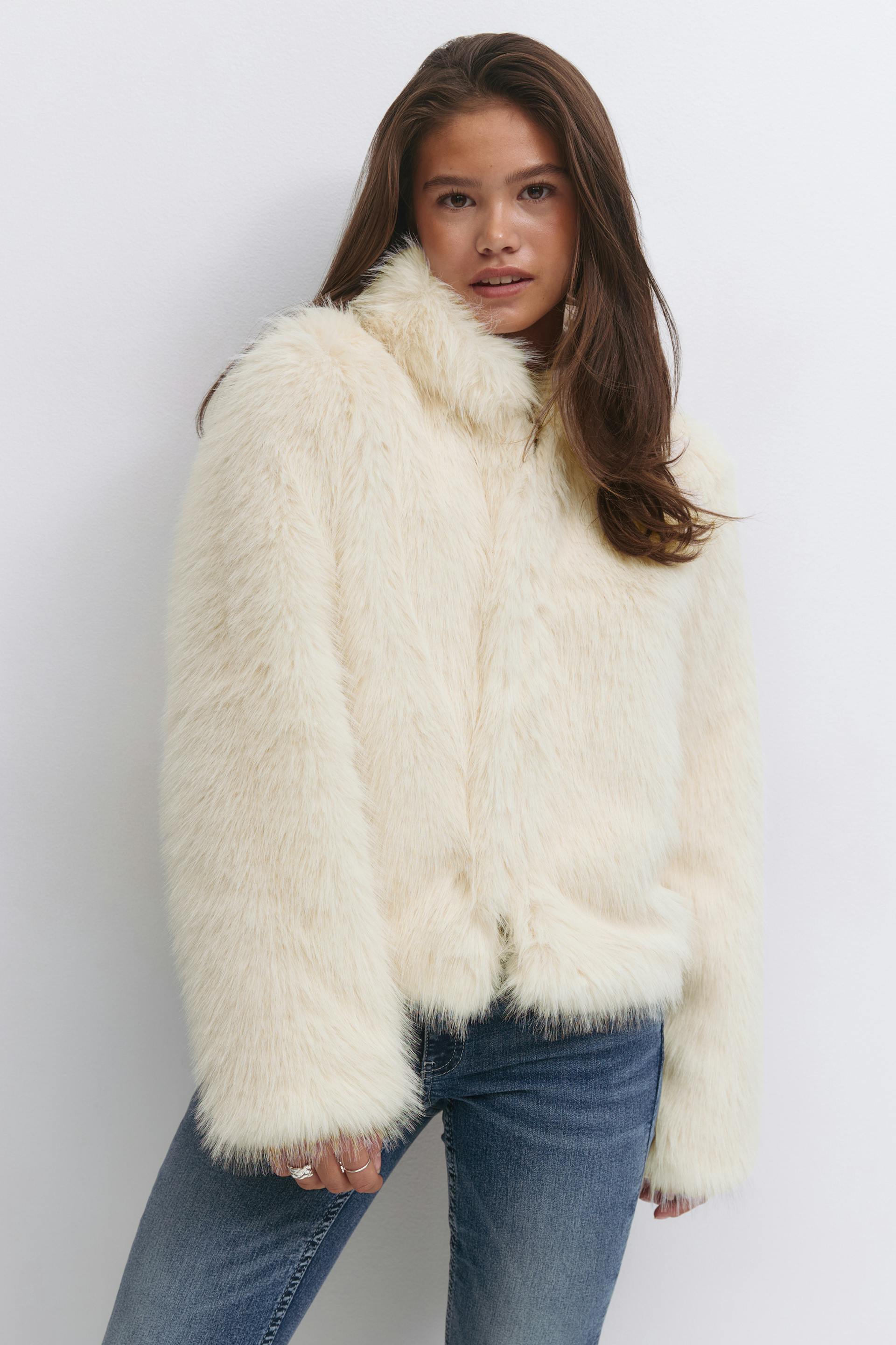 Ivory faux‑fur high‑collar jacket with long sleeves and slightly cropped hem, paired with medium‑wash blue jeans.