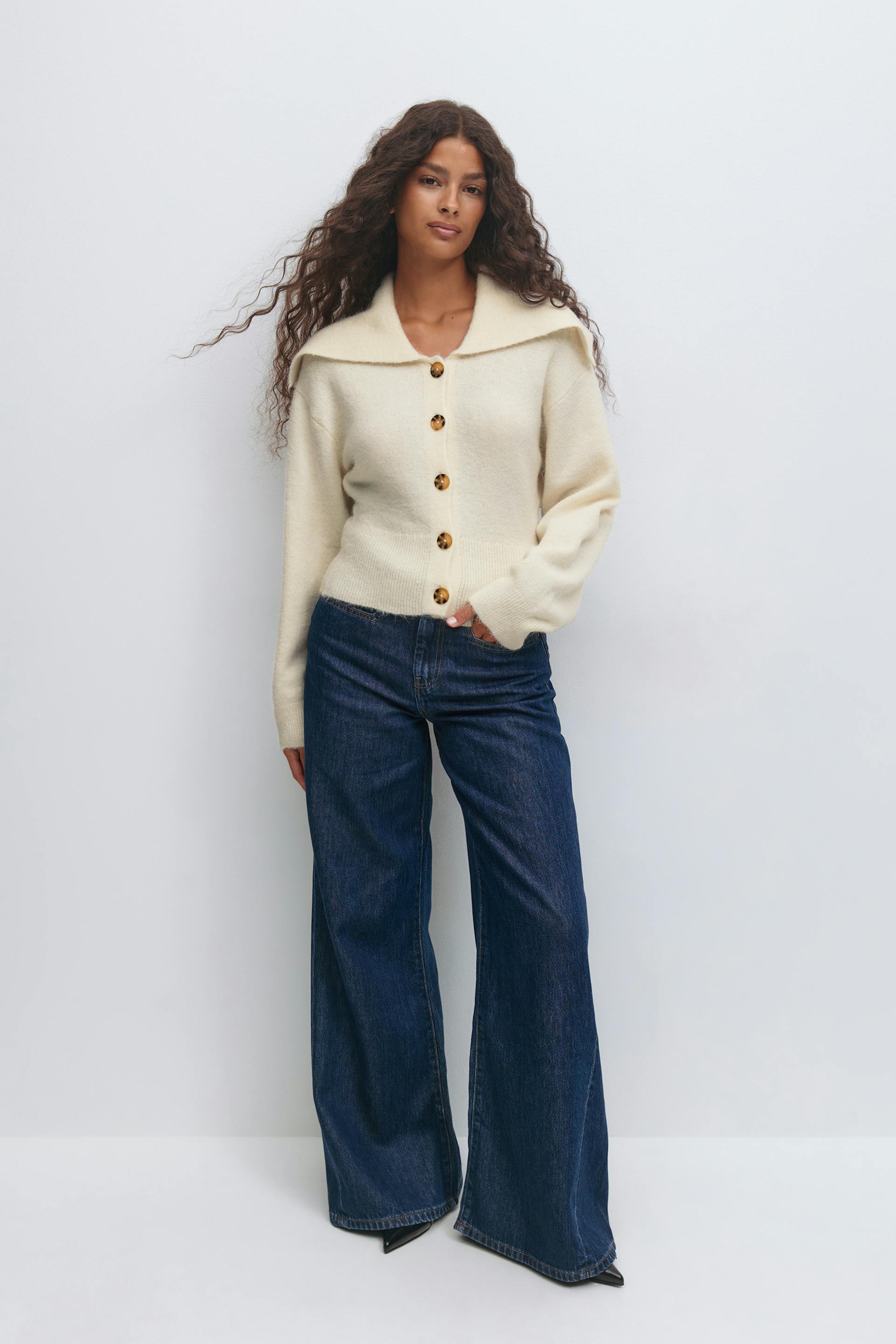 Cream knit button-up cardigan with a wide collar and tortoiseshell buttons, paired with dark indigo wide-leg jeans and black pointed-toe shoes.