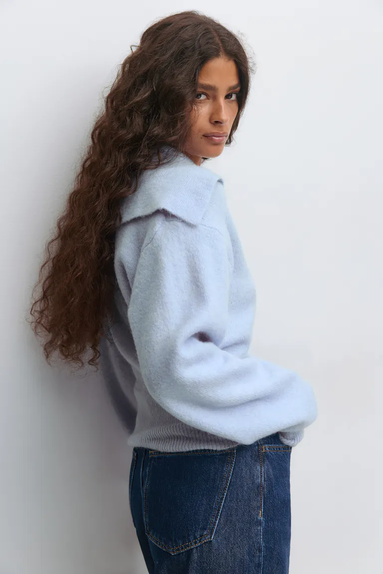 Hellblauer Langarmpullover aus gebürstetem Strick mit übergroßem, spitz zulaufendem Kragen und geripptem Saum, kombiniert mit dunkelblauen Denim-Jeans.