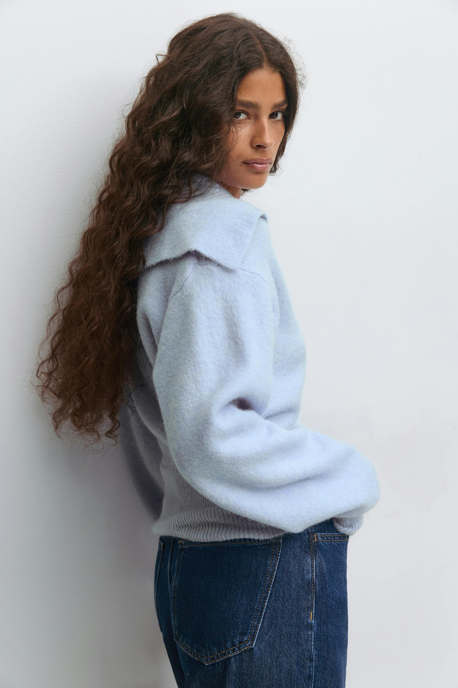 Hellblauer Langarmpullover aus gebürstetem Strick mit übergroßem, spitz zulaufendem Kragen und geripptem Saum, kombiniert mit dunkelblauen Denim-Jeans.