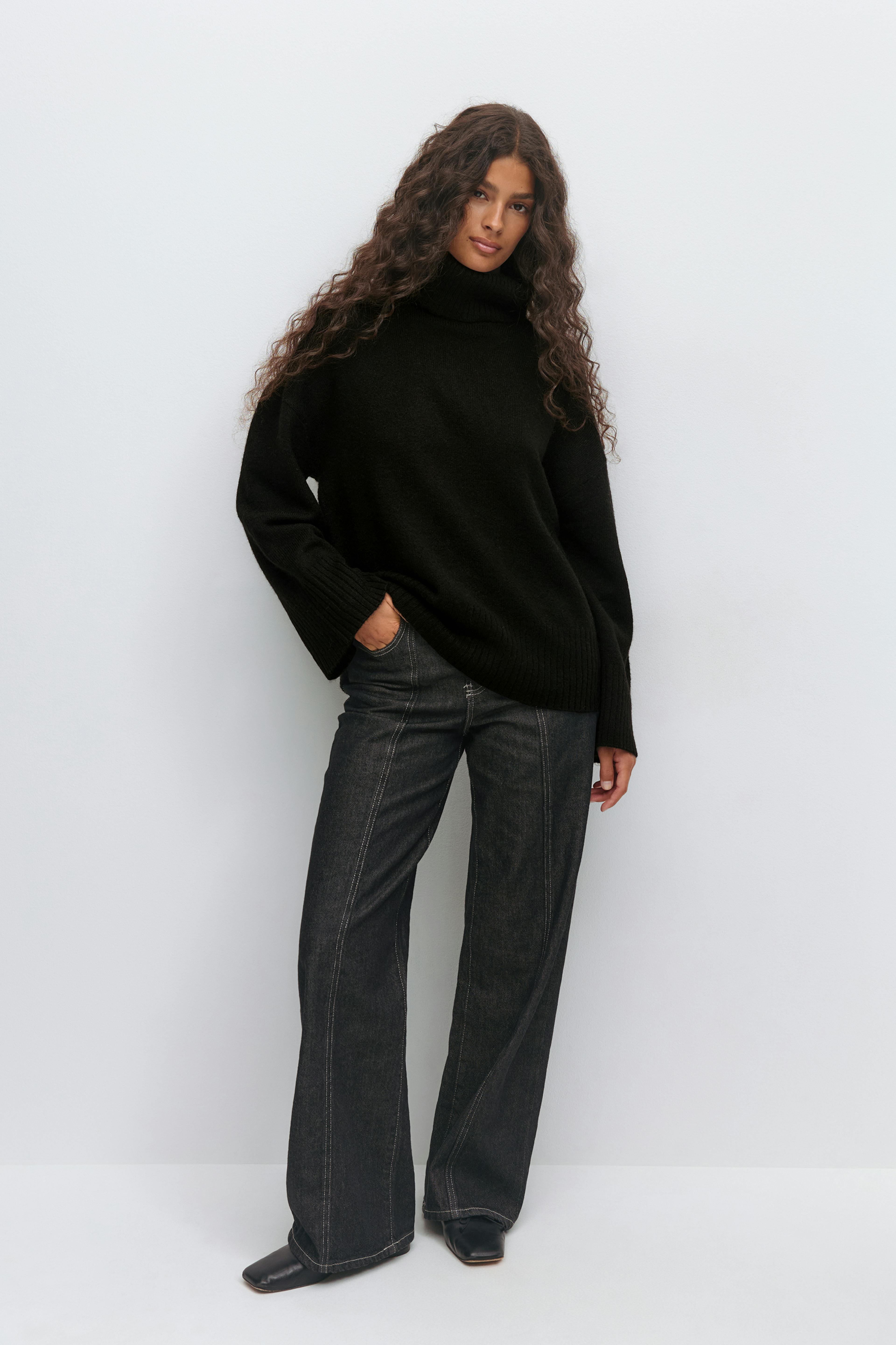 Black oversized turtleneck sweater with ribbed cuffs and hem, paired with dark-wash wide-leg jeans featuring front seam stitching and black square-toe ankle boots.