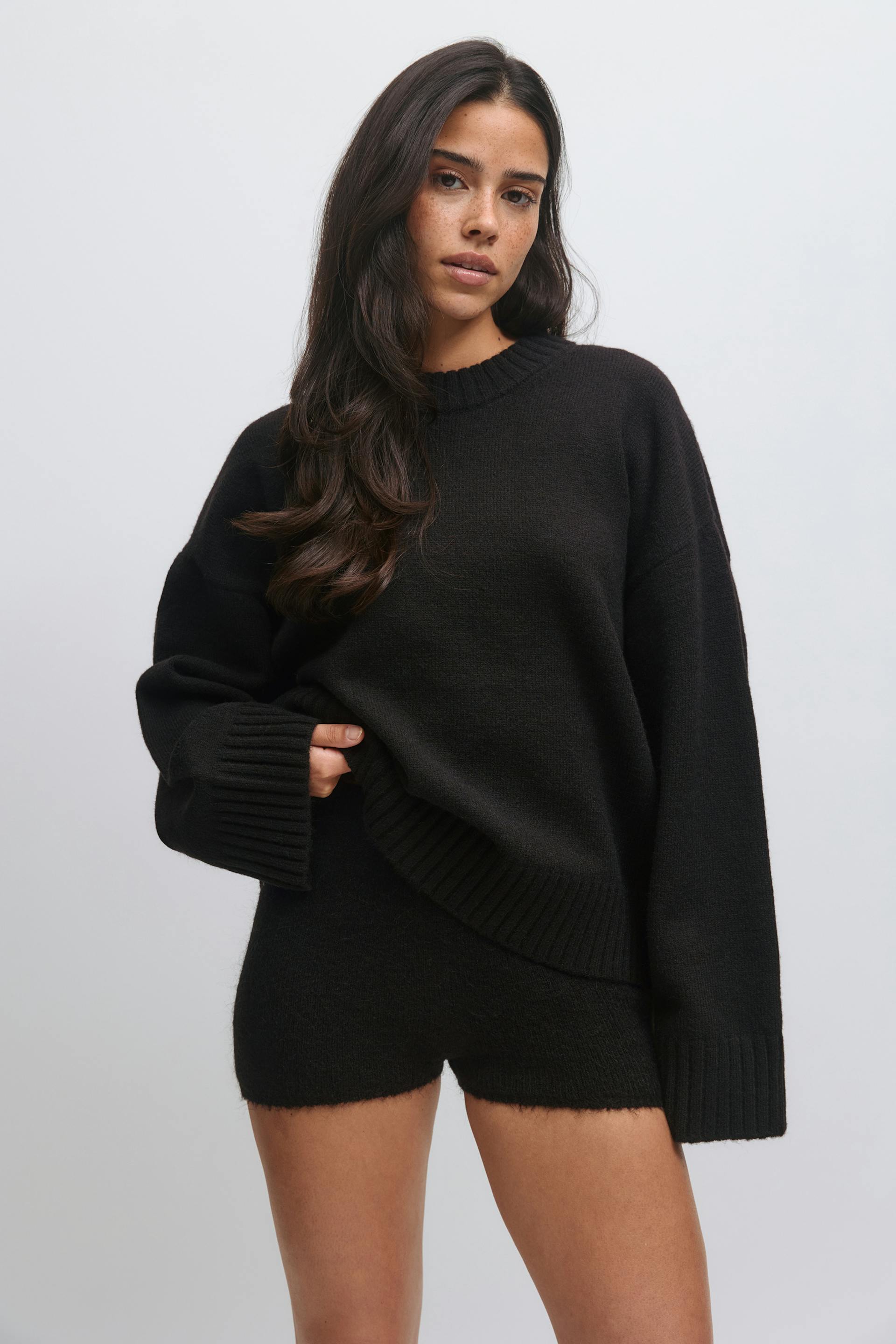 Musta ylisuuri, ylimitoitettu neulottu pusero, jossa on pitkät neulotut hihansuut ja helma, yhdistettynä yhteensopiviin mustiin neulotuihin shortseihin.