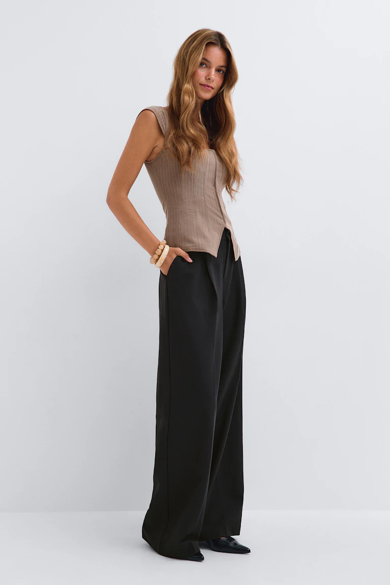 Kvinde iført en sort oversize blazer over en sort kort tanktop, med højtaljede sorte bukser med brede ben, et sort bælte med et ovalt sølvspænde og spidse sorte hæle.