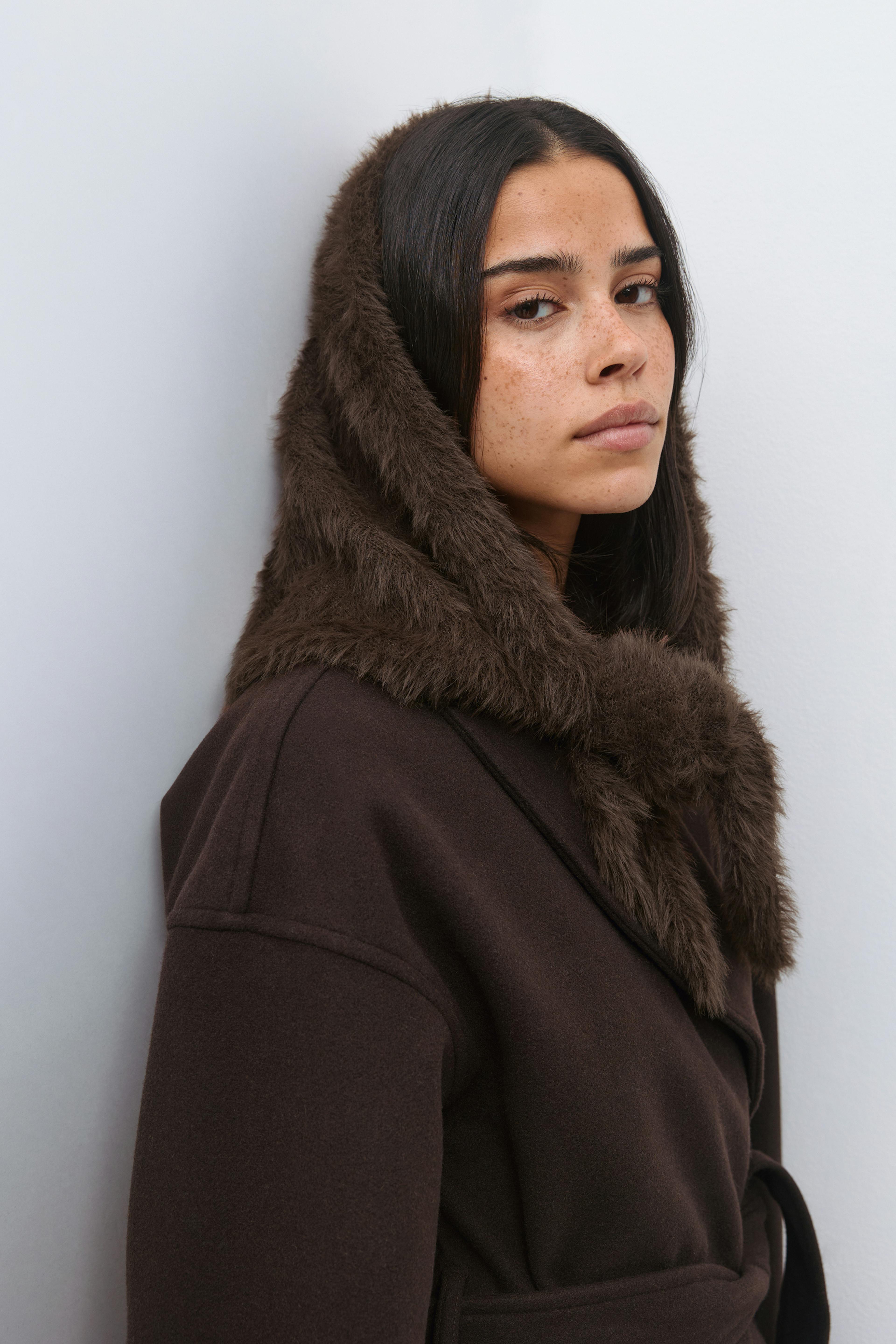 Manteau en laine marron foncé avec ceinture, capuche et bordures en fausse fourrure.