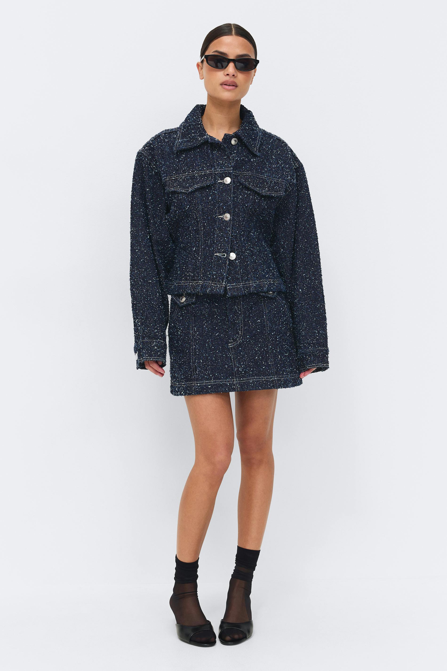Navy speckled tweed button-front boxy jacket with matching mini skirt, styled with narrow black sunglasses, sheer black ankle socks and black open-toe mules.