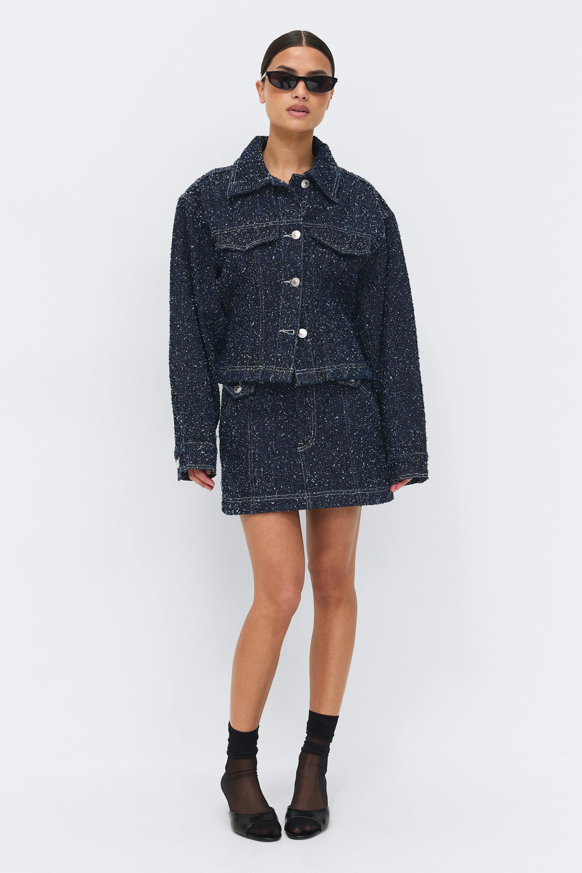 Navy speckled tweed button-front boxy jacket with matching mini skirt, styled with narrow black sunglasses, sheer black ankle socks and black open-toe mules.