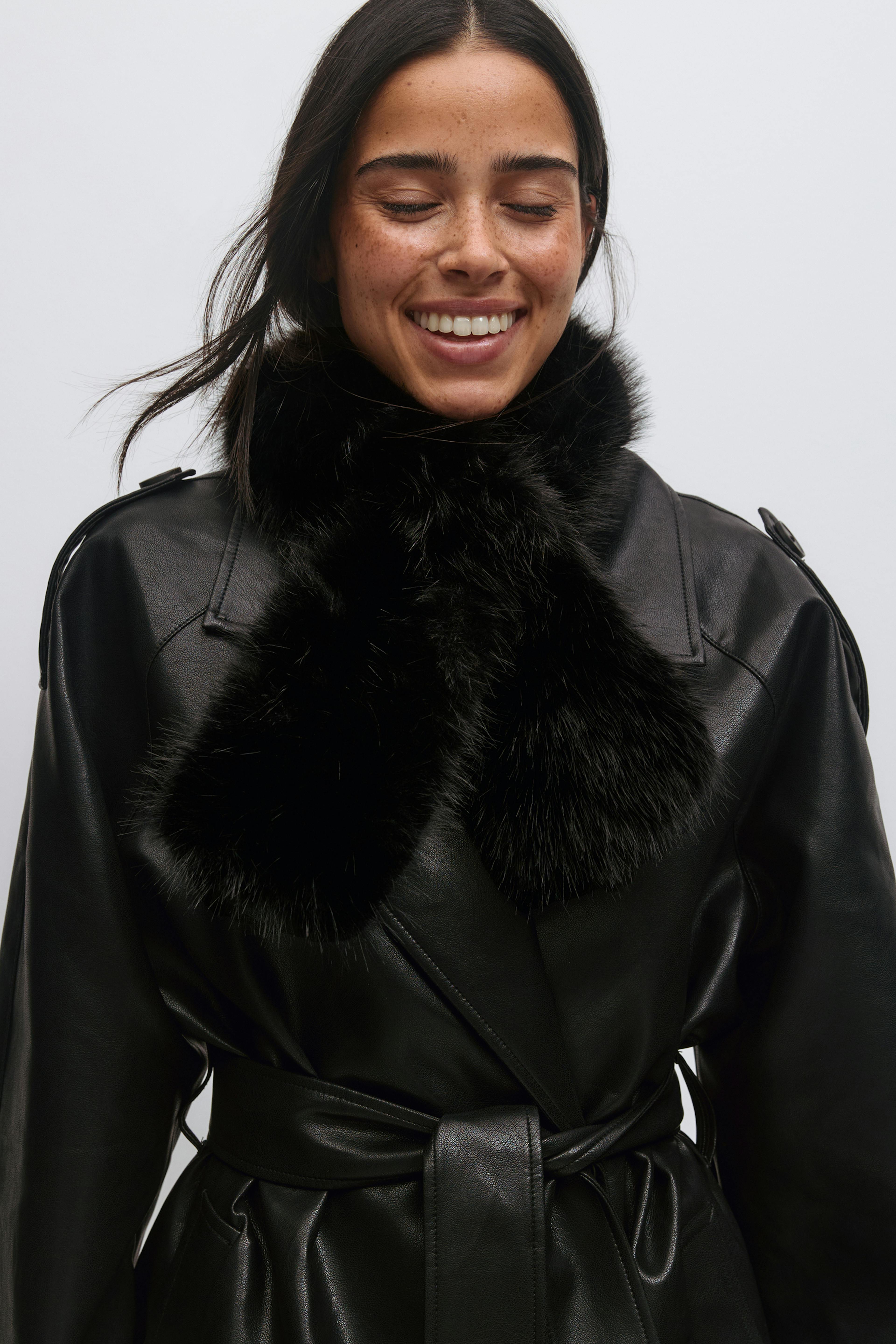 Trench en cuir noir ceinturé à larges revers, associé à une écharpe en fourrure noire en peluche.
