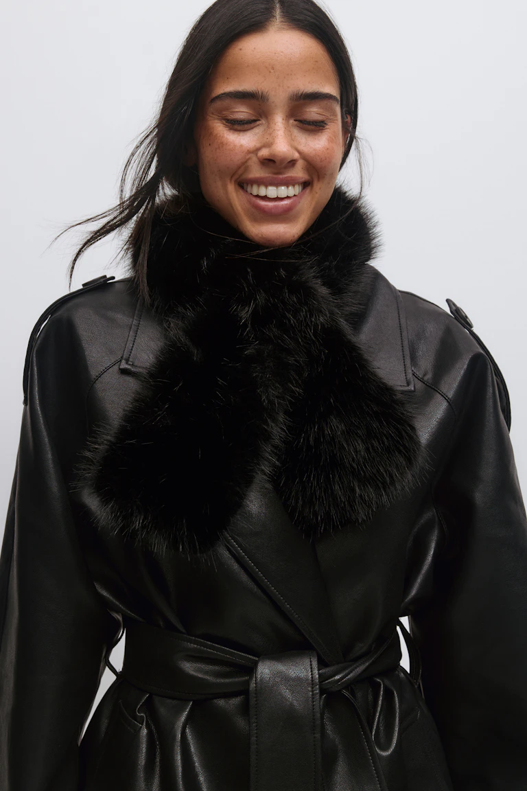 Black belted leather trench coat with wide lapels, paired with a plush black fur neck scarf.