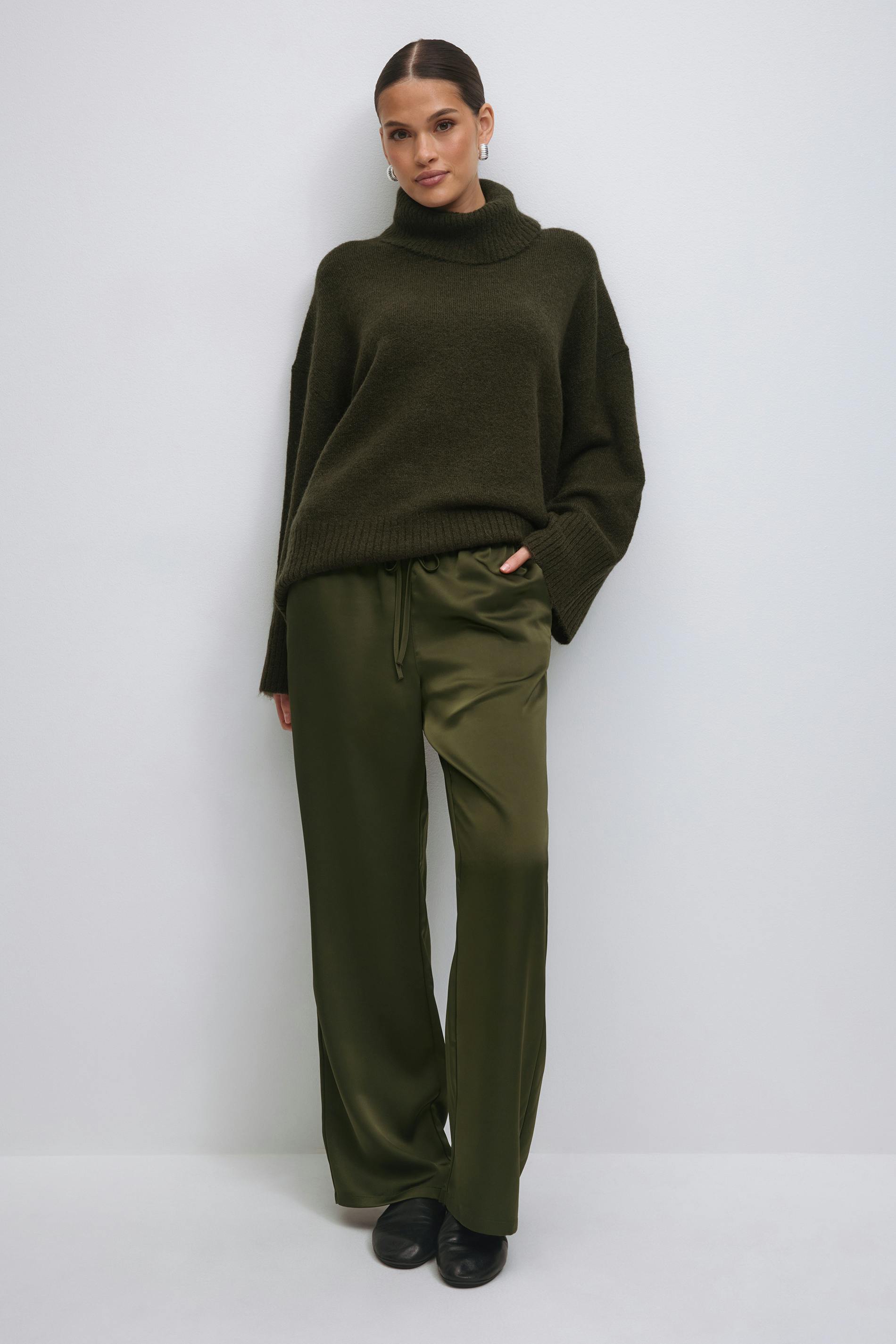 White sleeveless peplum top paired with olive-green satin wide-leg drawstring trousers and cream pleated ballet flats.