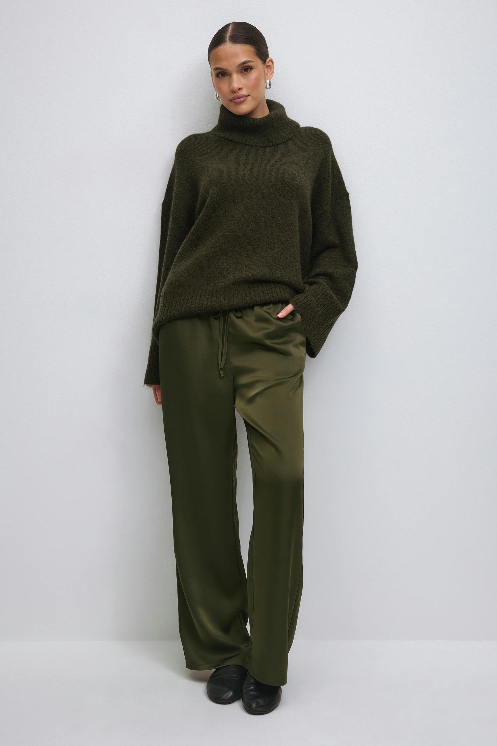 White sleeveless peplum top paired with olive-green satin wide-leg drawstring trousers and cream pleated ballet flats.