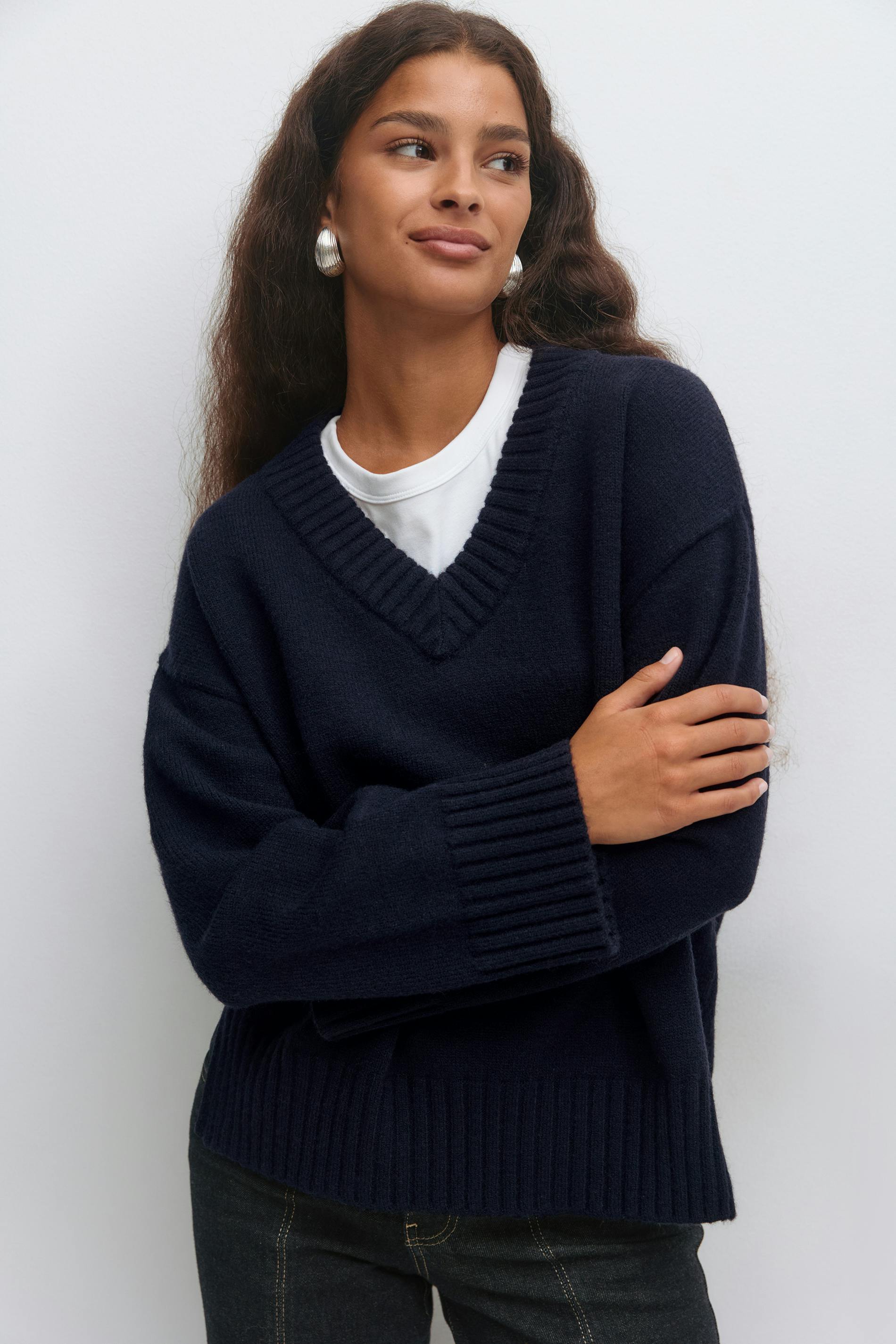 Navy sweater med V-hals over en hvid T-shirt med rund hals, mørke denimjeans og sølvfarvede øreringe.