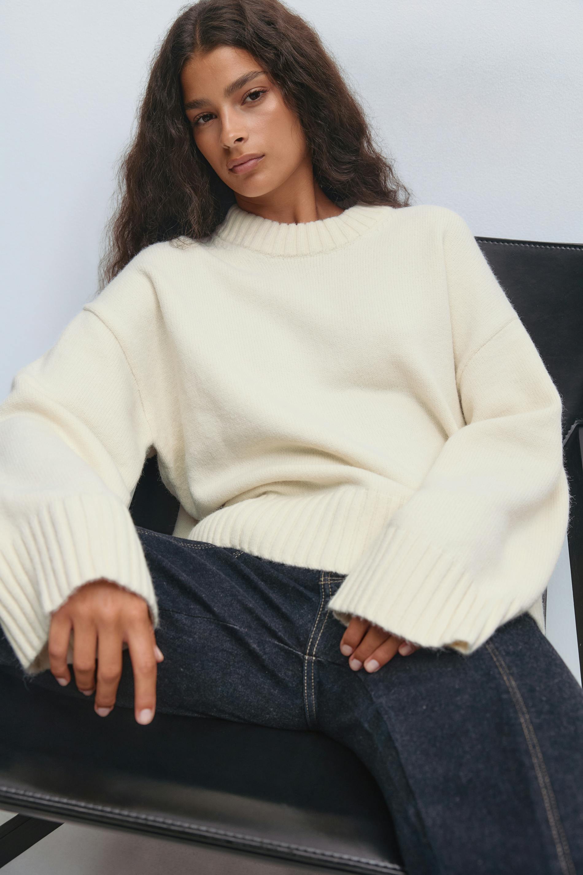 Crème oversized geribde crewneck trui met verlengde geribde boorden en zoom, gecombineerd met een donkere indigo jeans met contrasterende stiksels.